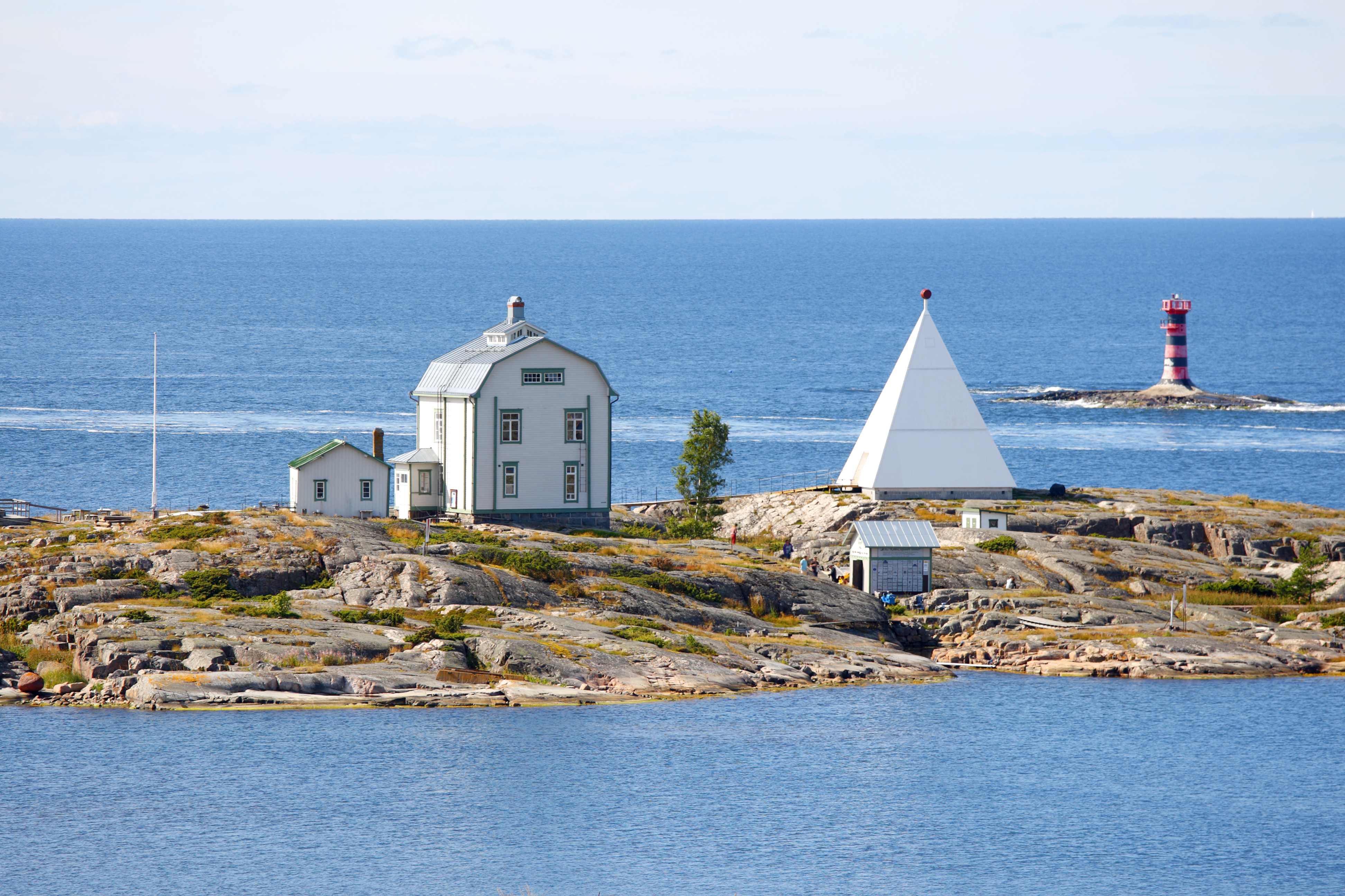 Idyllisk klippeø med historisk lodsestation og hvid pyramide i Ålands skærgård ved Østersøen om sommeren