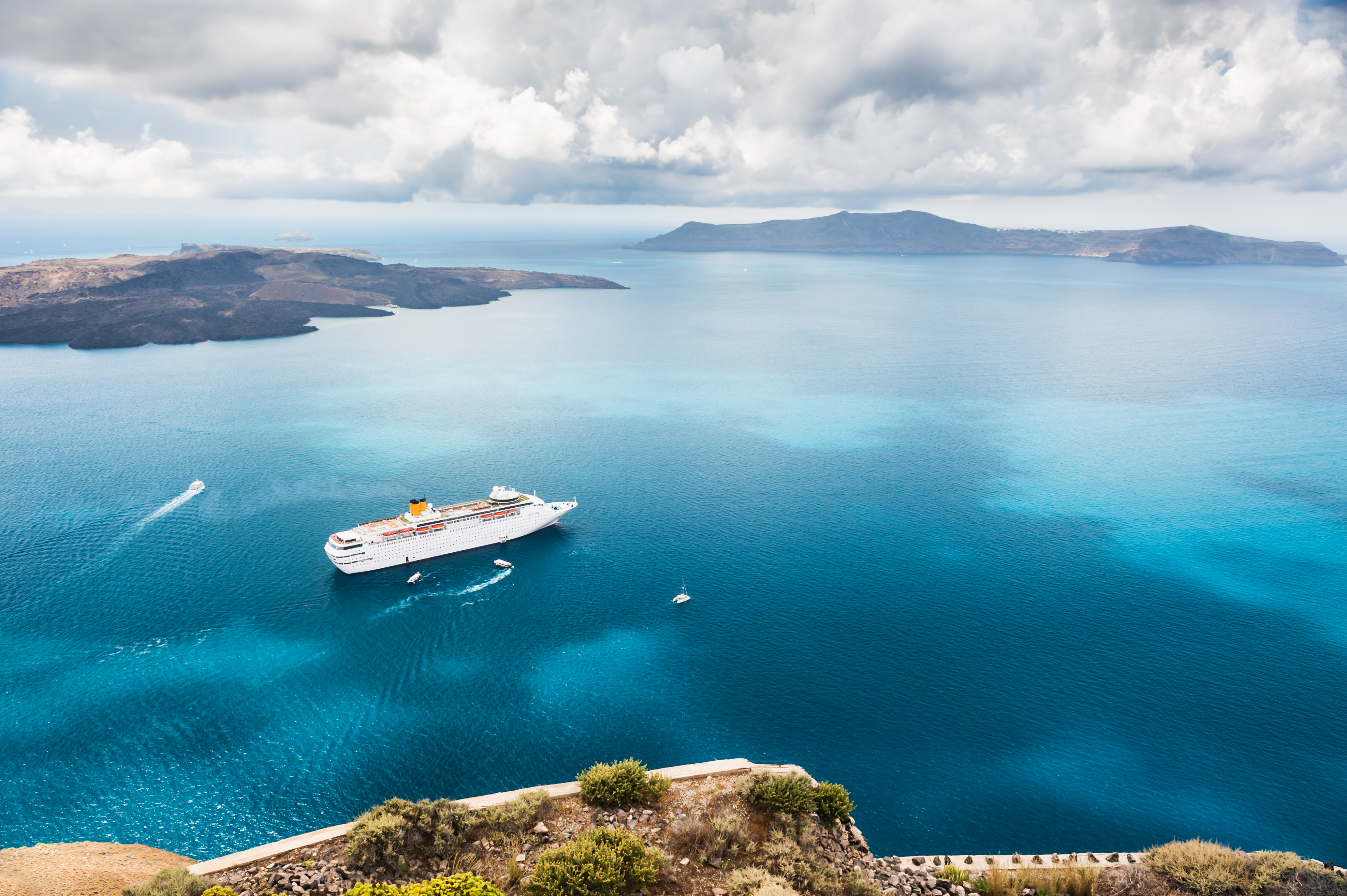 Hvidt krydstogtskib i det azurblå Ægæiske Hav ved Santorini med bjerglandskab