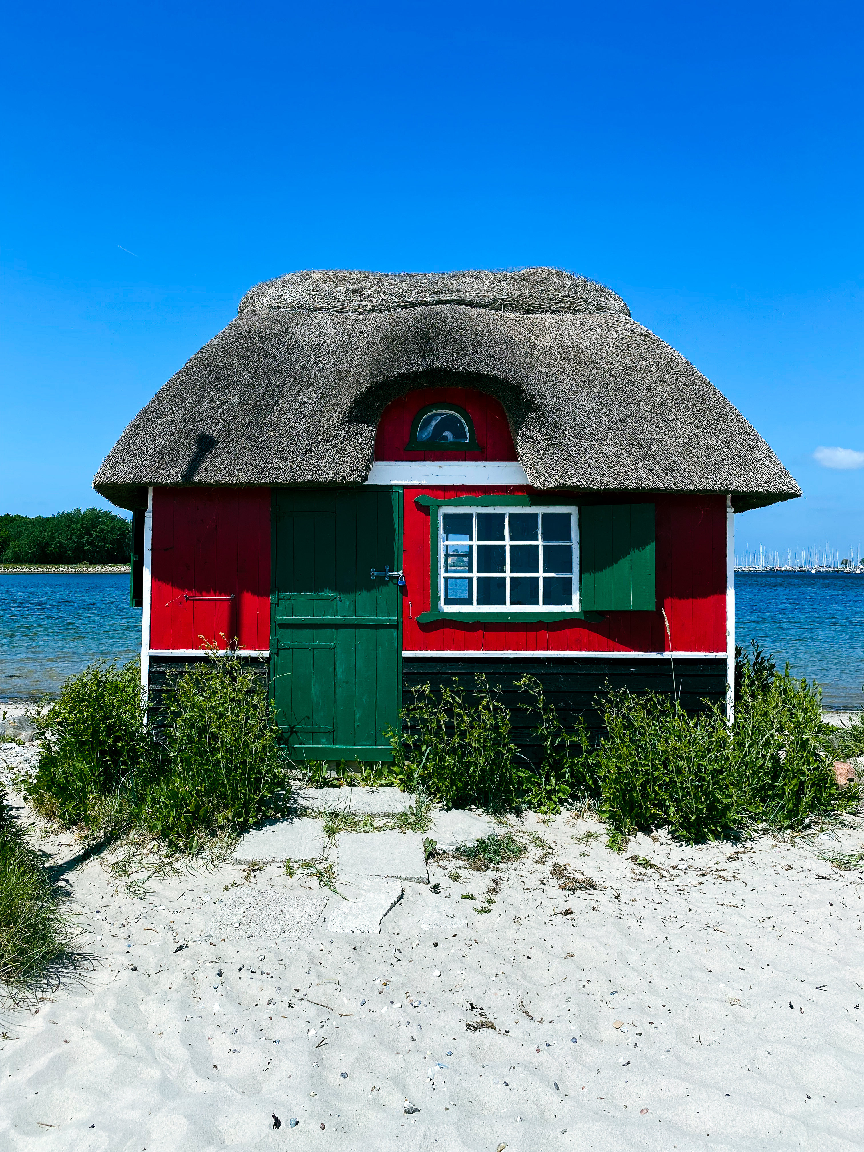 Hyggeligt rødt sommerhus med stråtag direkte på stranden på den idylliske ø Ærø under den blå danske sommerhimmel
