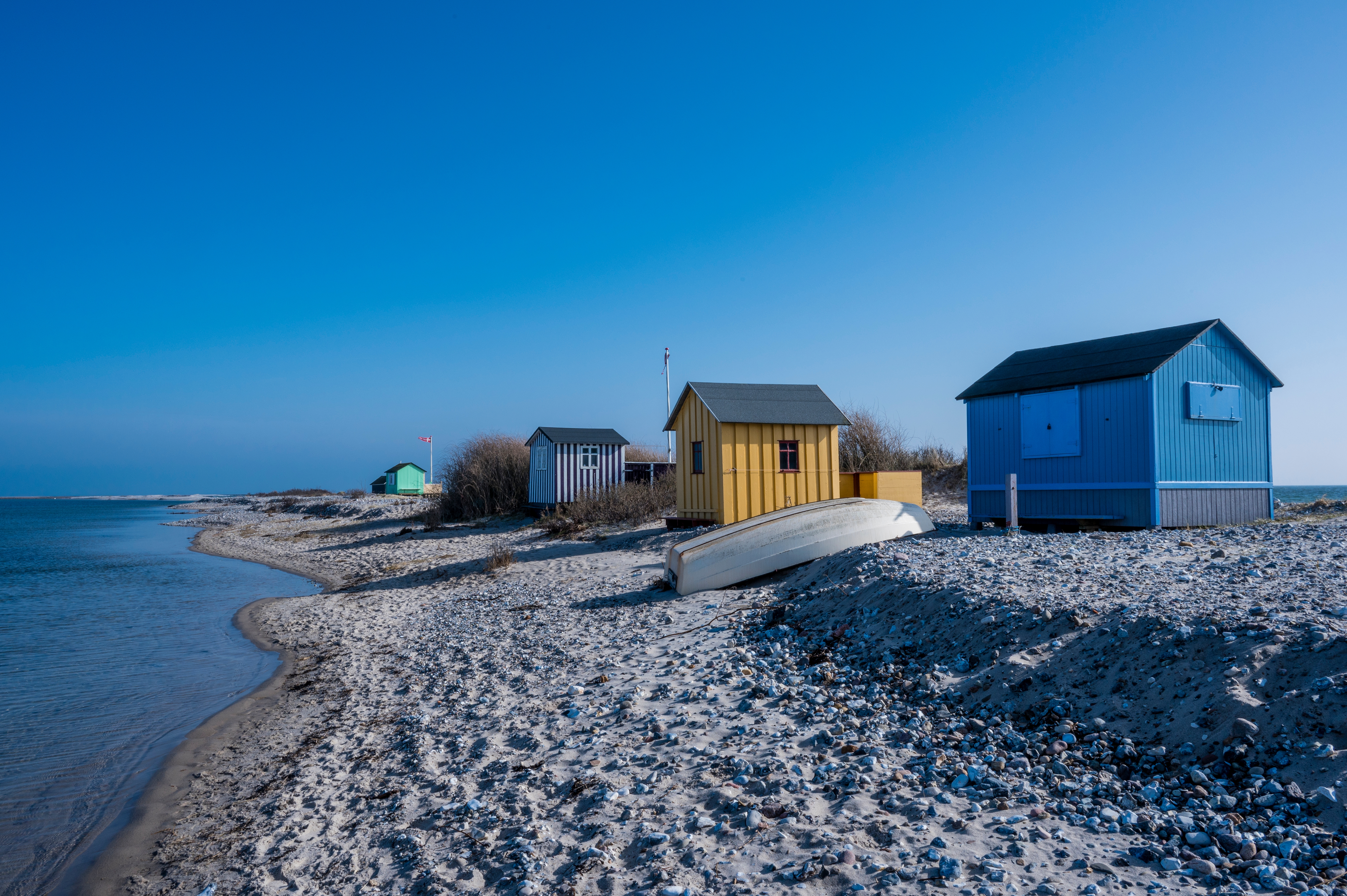 Maleriske badehuse på Ærøs stenstrand nær Rudkøbing med blå himmel og roligt hav på en solrig dag