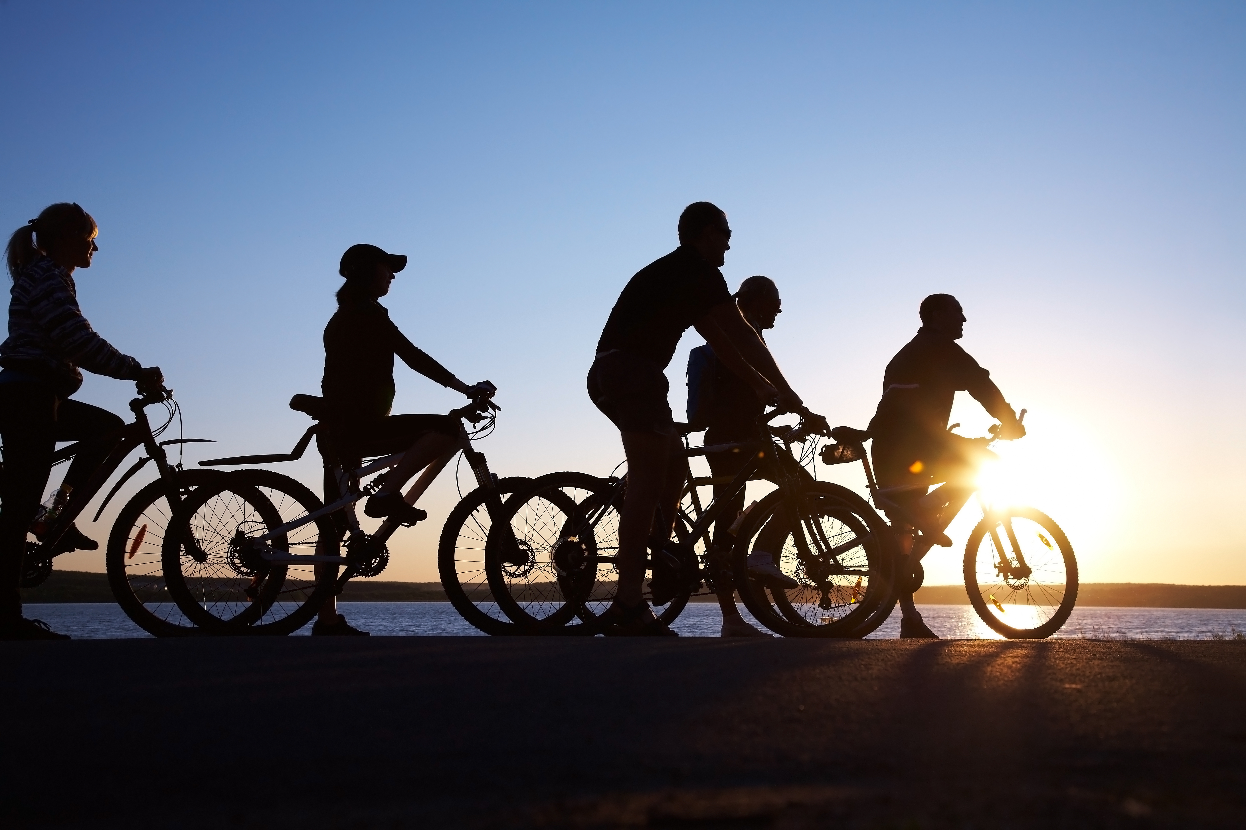 Silhuetter af en gruppe venner på cykler mod den gyldne solnedgang ved vandet - oplev frihed og fællesskab på aktive ferierejser med Nille Rejser