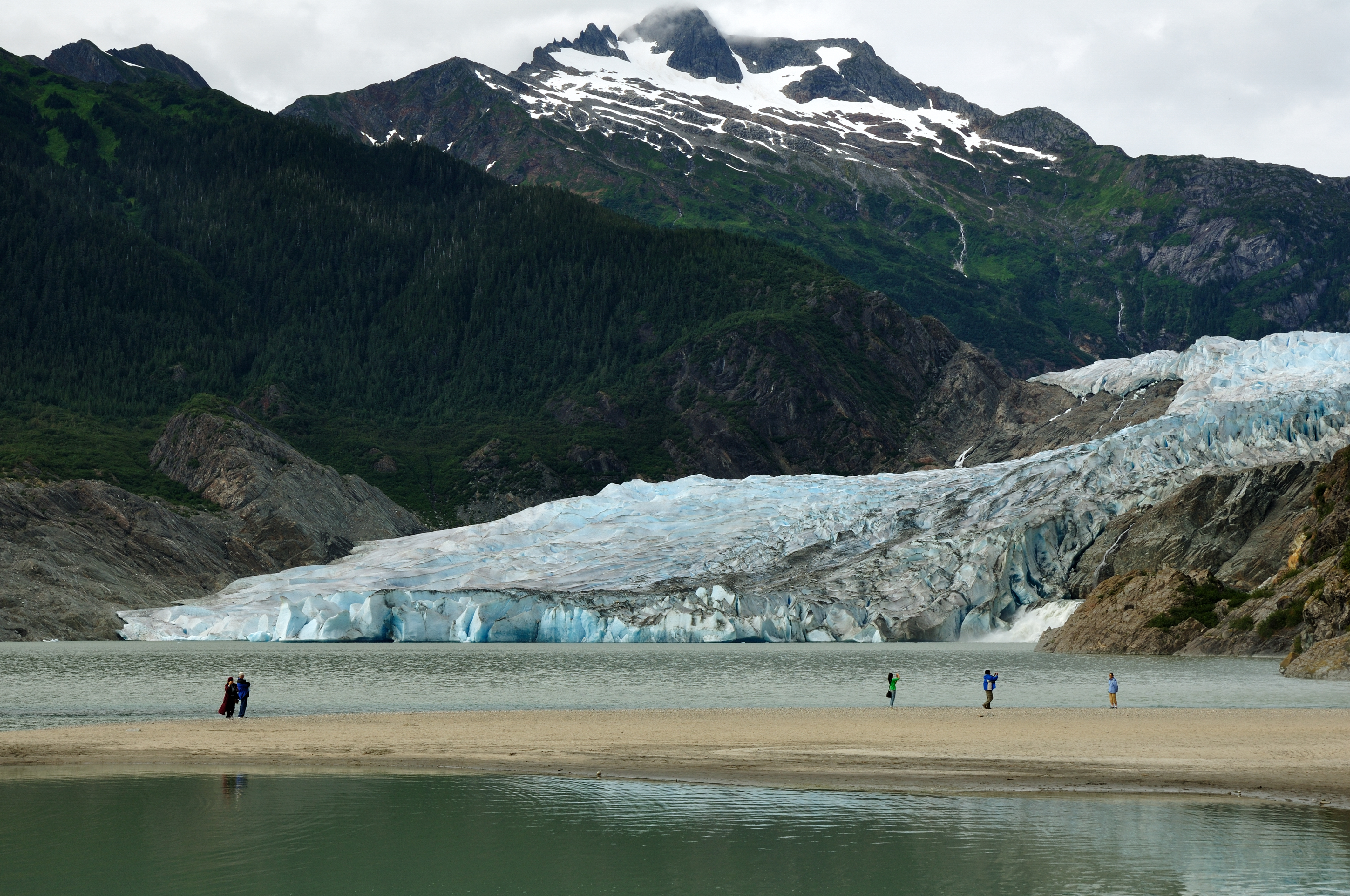 Alaska gletsjer strand med turister og sne-toppede bjerge i baggrunden