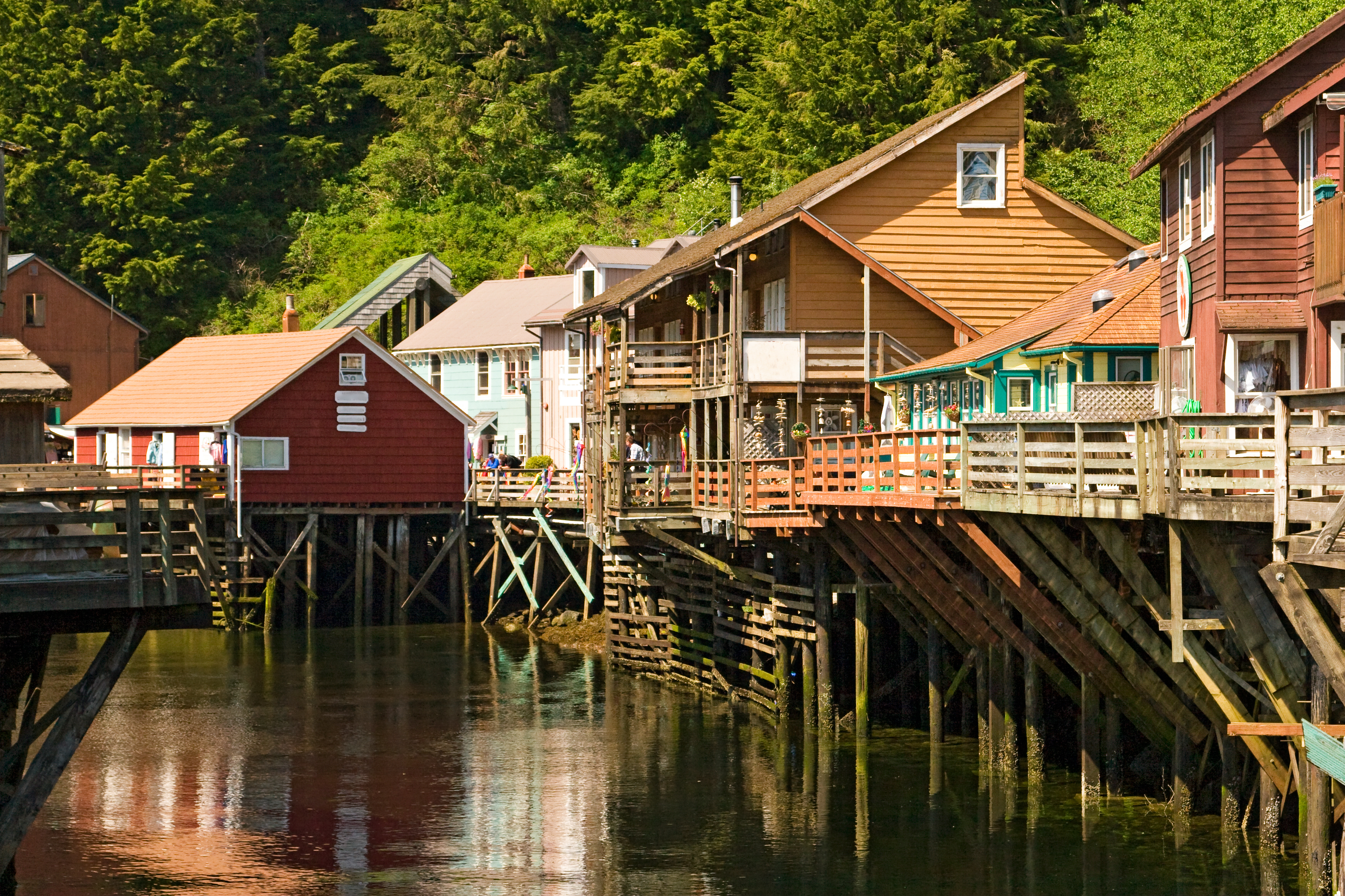Maleriske farverige træhuse på pæle langs Creek Street i Ketchikan, Alaska med skov i baggrunden