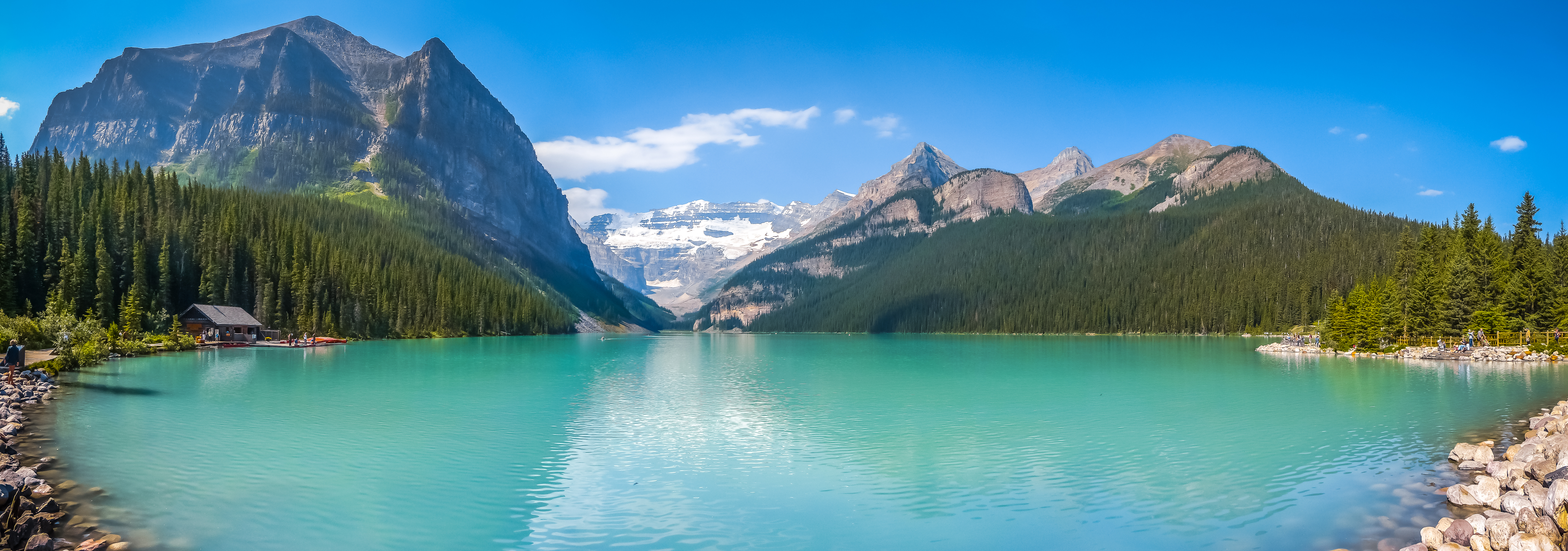 Idyllisk sommerudsigt over den smukke Lake Louise med sin karakteristiske turkise farve, omgivet af majestætiske bjerge og grønne skove i Banff National Park, Alberta, Canada