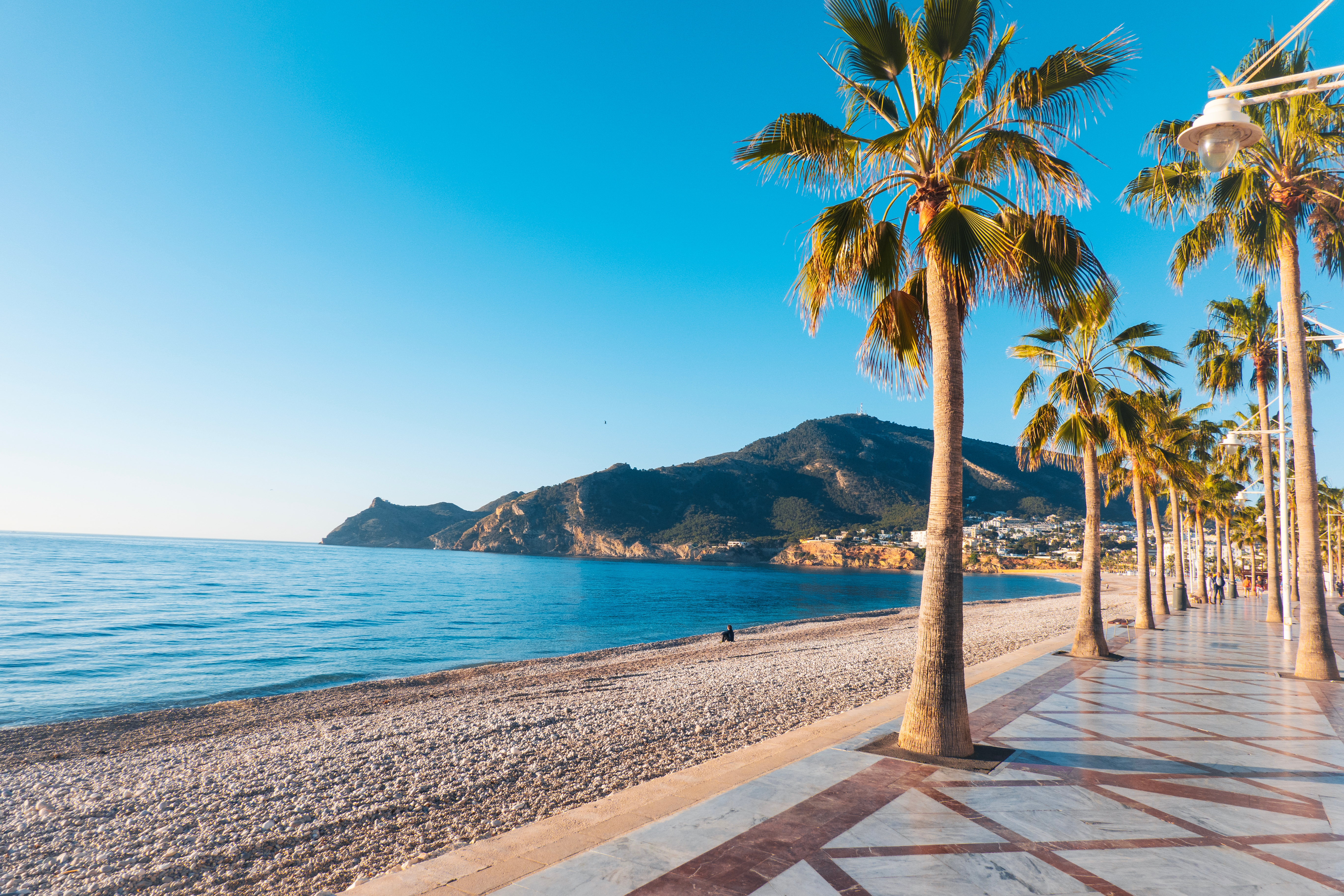 Dejlig strandpromenade i Albir med palmer og roligt Middelhav omgivet af bjerge nær Benidorm og Altea på Costa Blanca