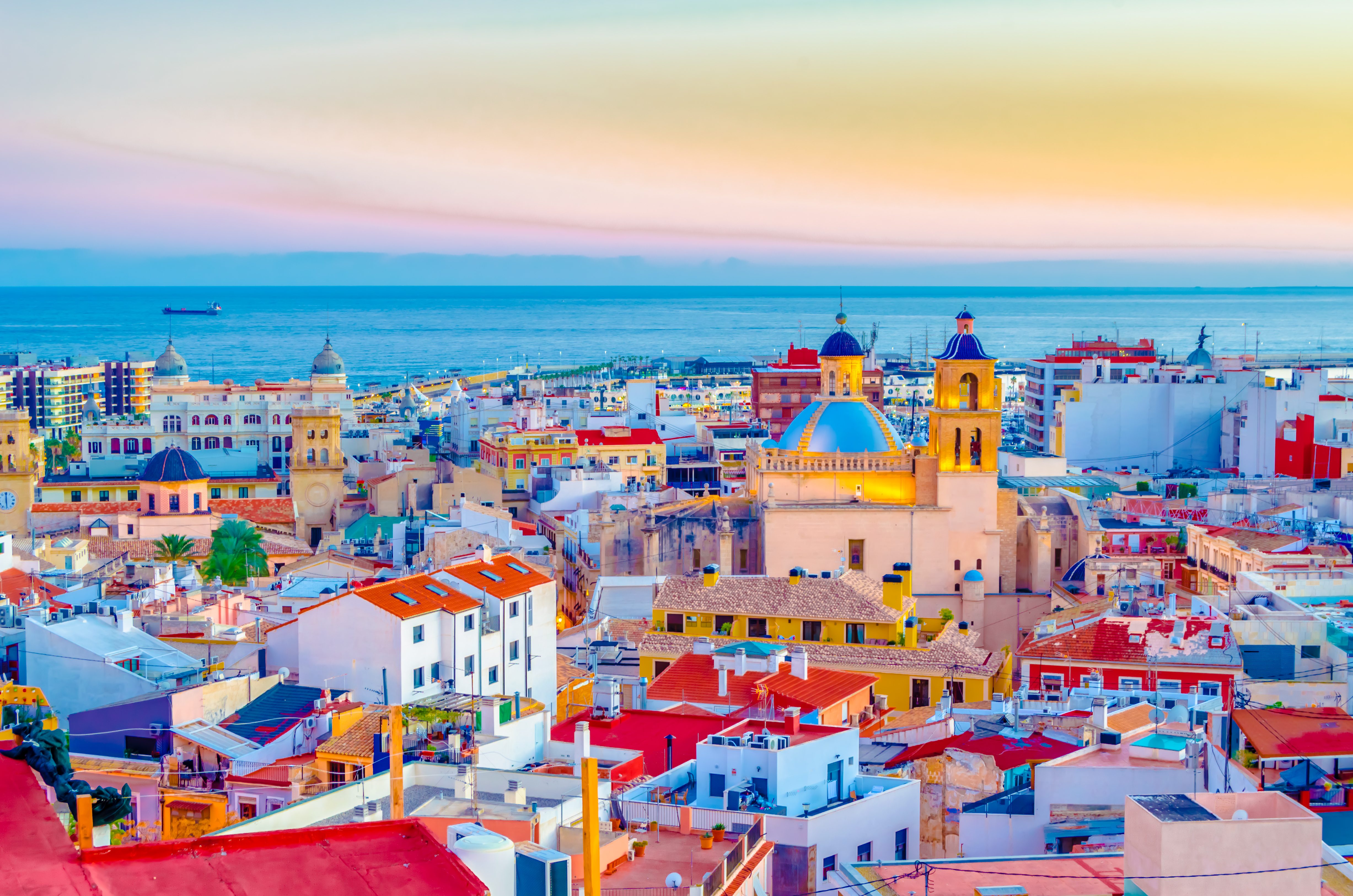 Farverig udsigt over Alicantes bymidte i skumringen med den smukke katedral med blå kuppel og det rolige Middelhav i horisonten på Costa Blanca, Spanien