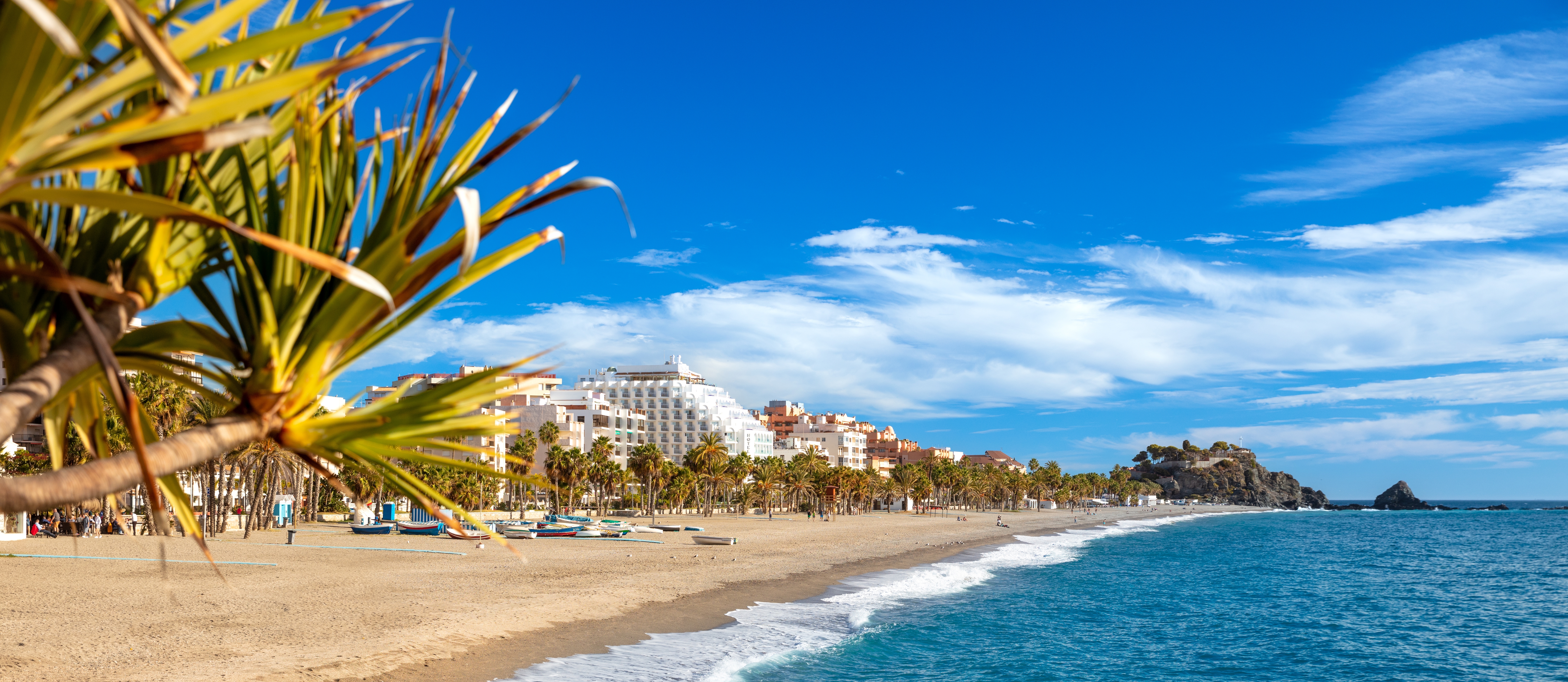 Malerisk udsigt over strandpromenaden med palmer og den brede sandstrand i den charmerende ferieby Almuñécar ved Andalusiens kyst