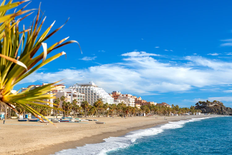 Malerisk udsigt over strandpromenaden med palmer og den brede sandstrand i den charmerende ferieby Almuñécar ved Andalusiens kyst