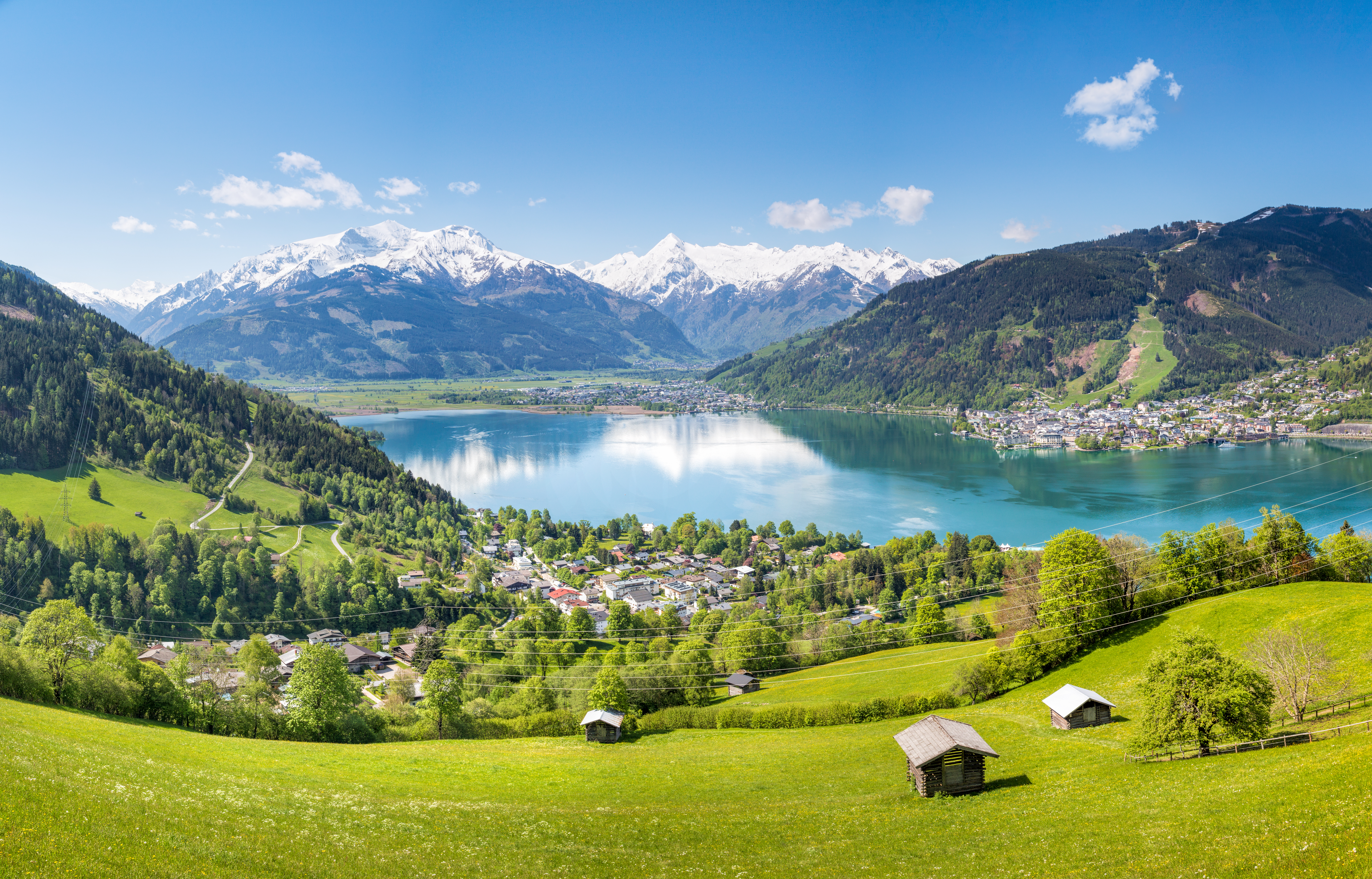 Storslået sommerpanorama over den østrigske feriedestination Zell am See med den blå bjergø, grønne alpeenge og den hyggelige by indrammmet af høje bjergtinder