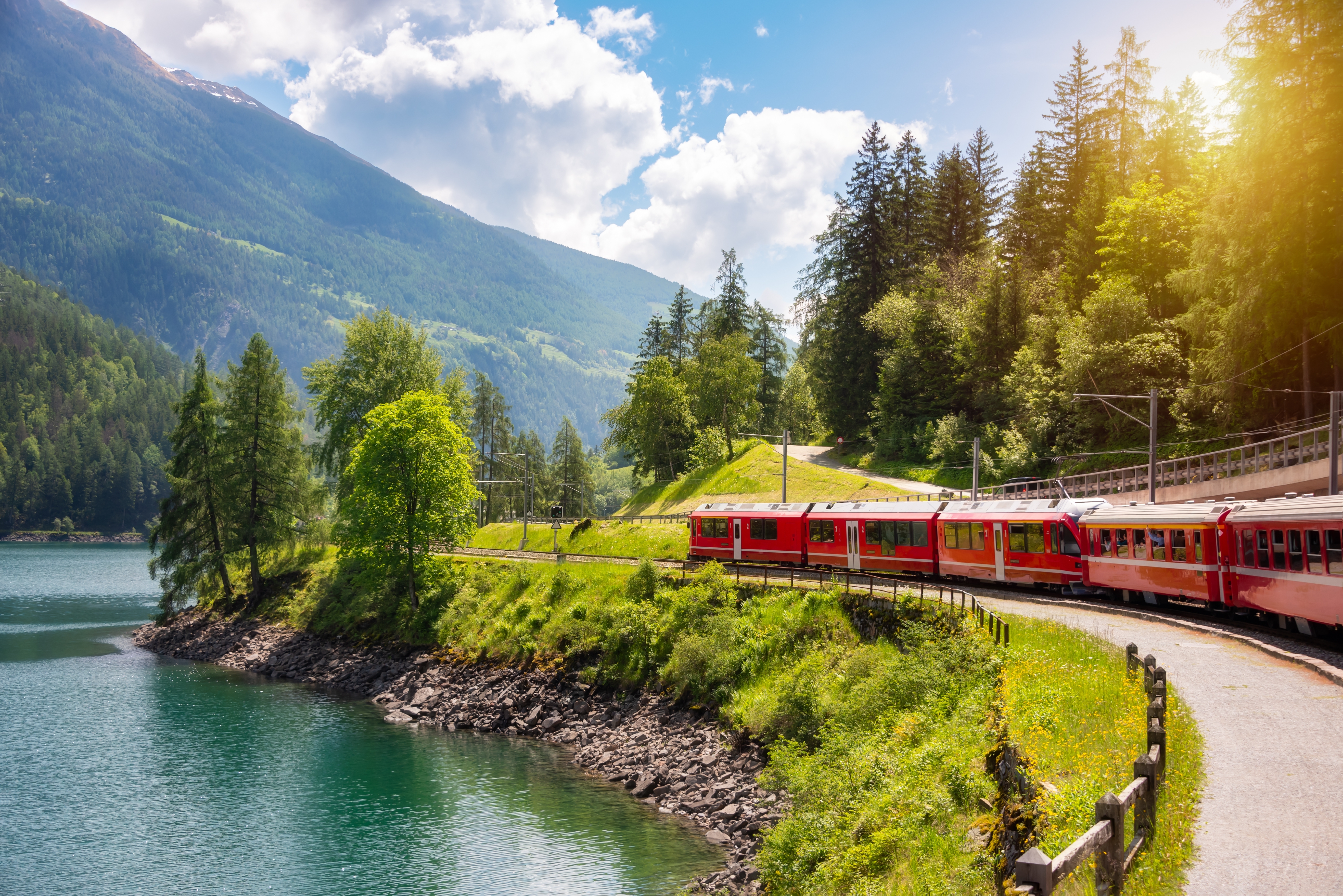 Berømt rødt Bernina Express tog på vej gennem spektakulær schweizisk natur med bjerge, skov og azurblå sø
