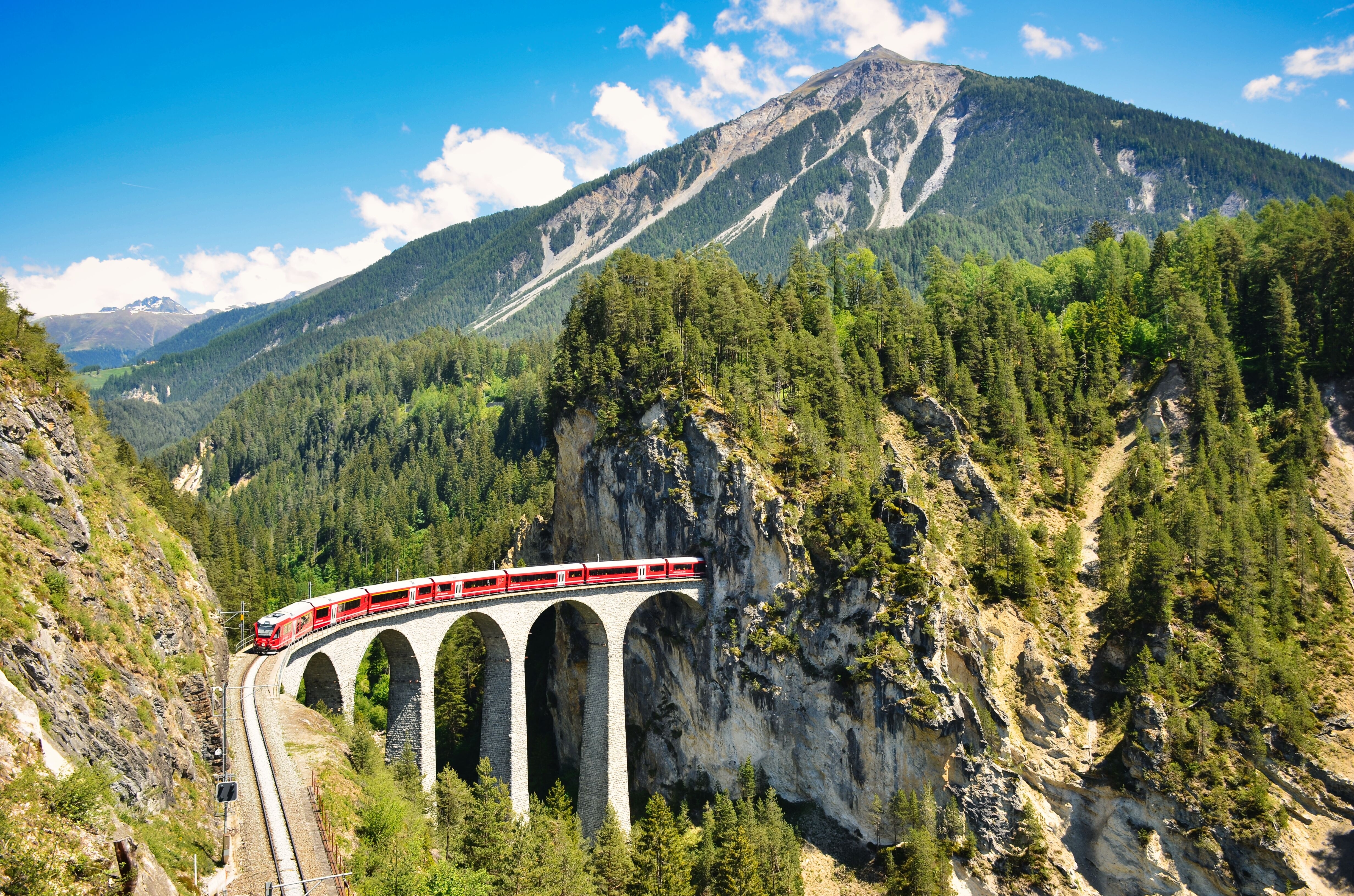 Ikonisk rødt tog på schweizisk viaduktbro med fantastisk udsigt over Alpernes grønne bjerge og skove