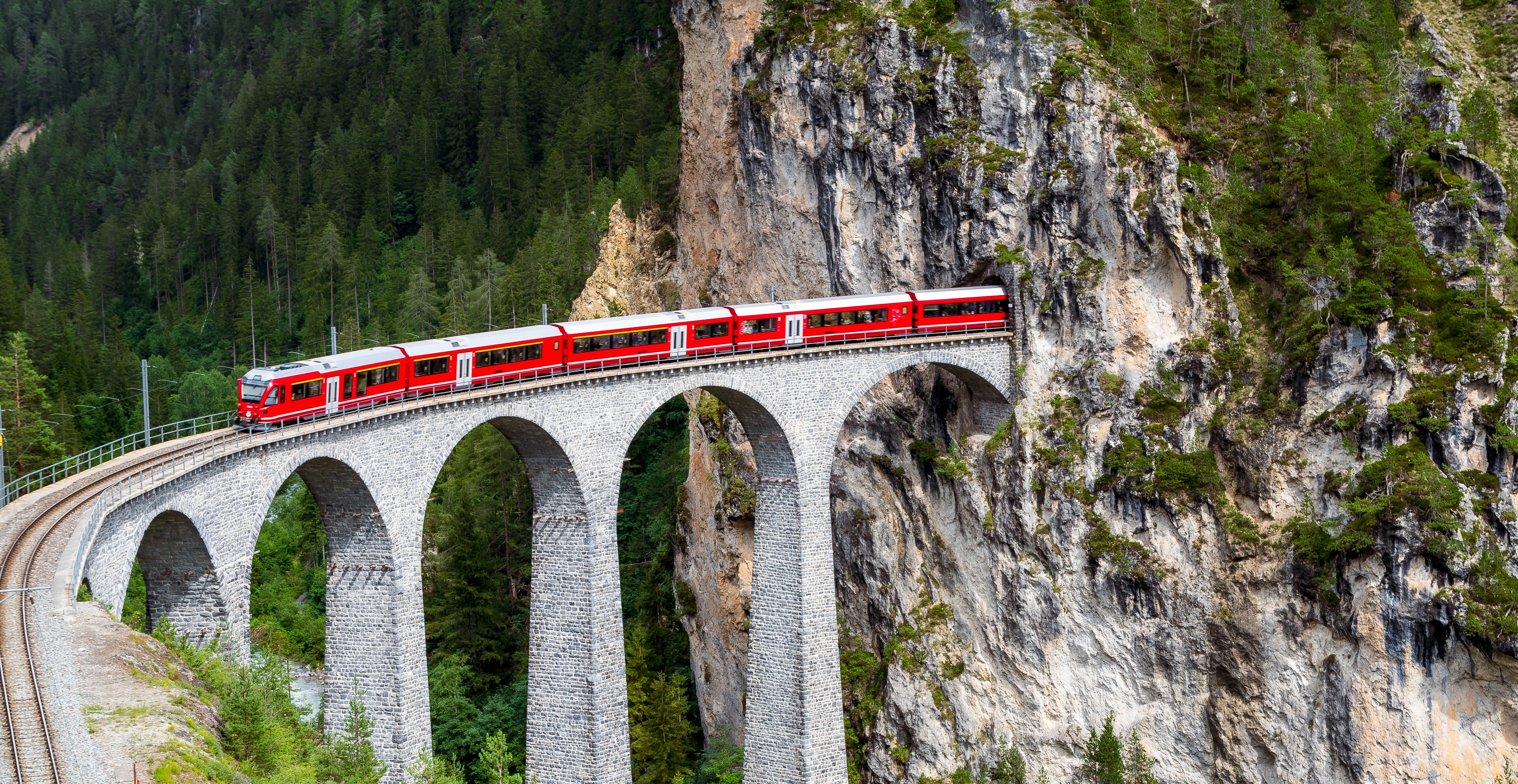 Rød alpetog krydser imponerende stenbridge i de schweiziske alper