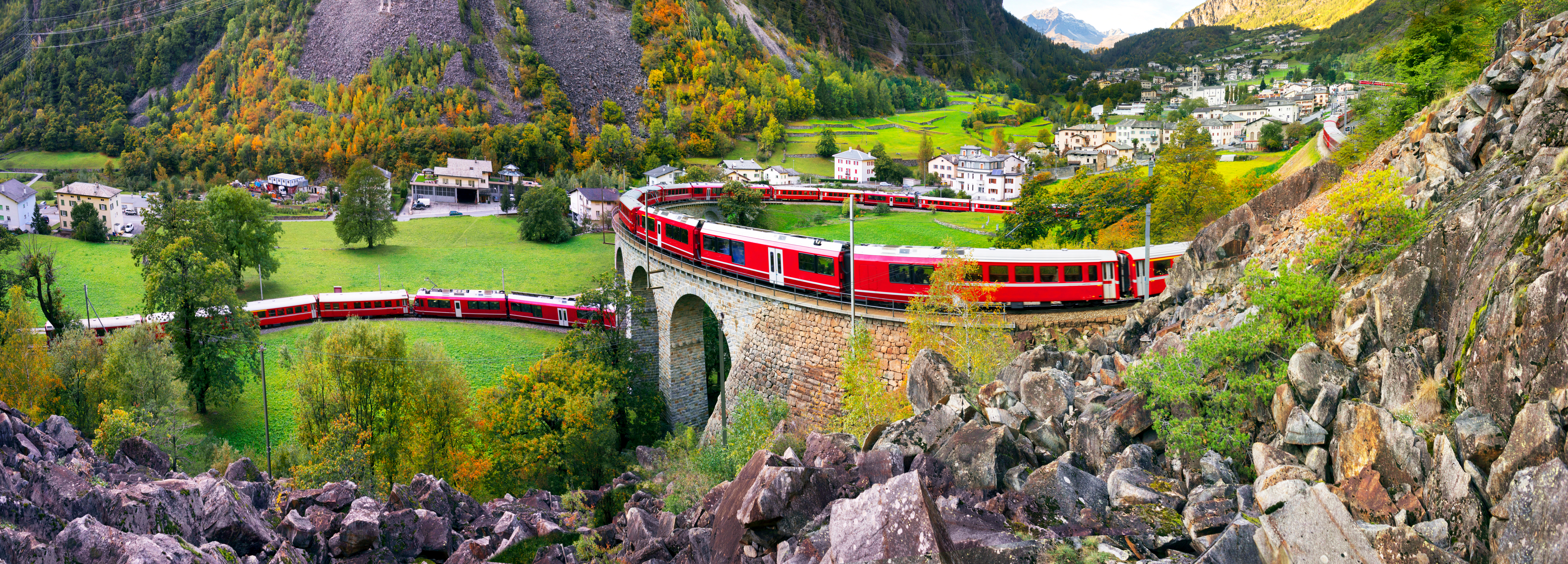 Alpine togrejse med rødt tog over viadukt i schweiziske bjerge