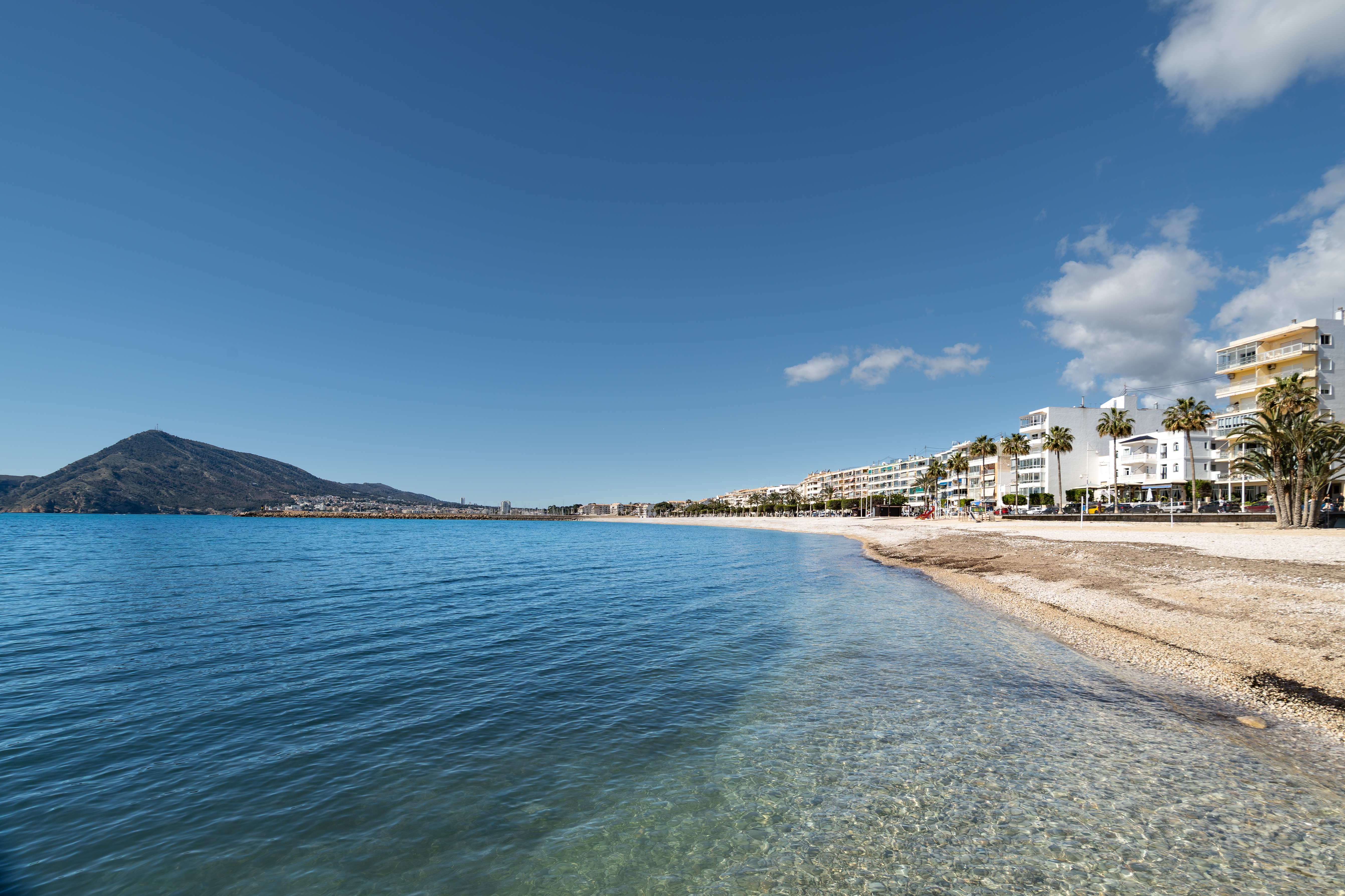 Idyllisk kystlinje i Altea på den spanske Costa Blanca med klart turkist Middelhavsvand, stenstrand og hvide bygninger under en strålende blå himmel