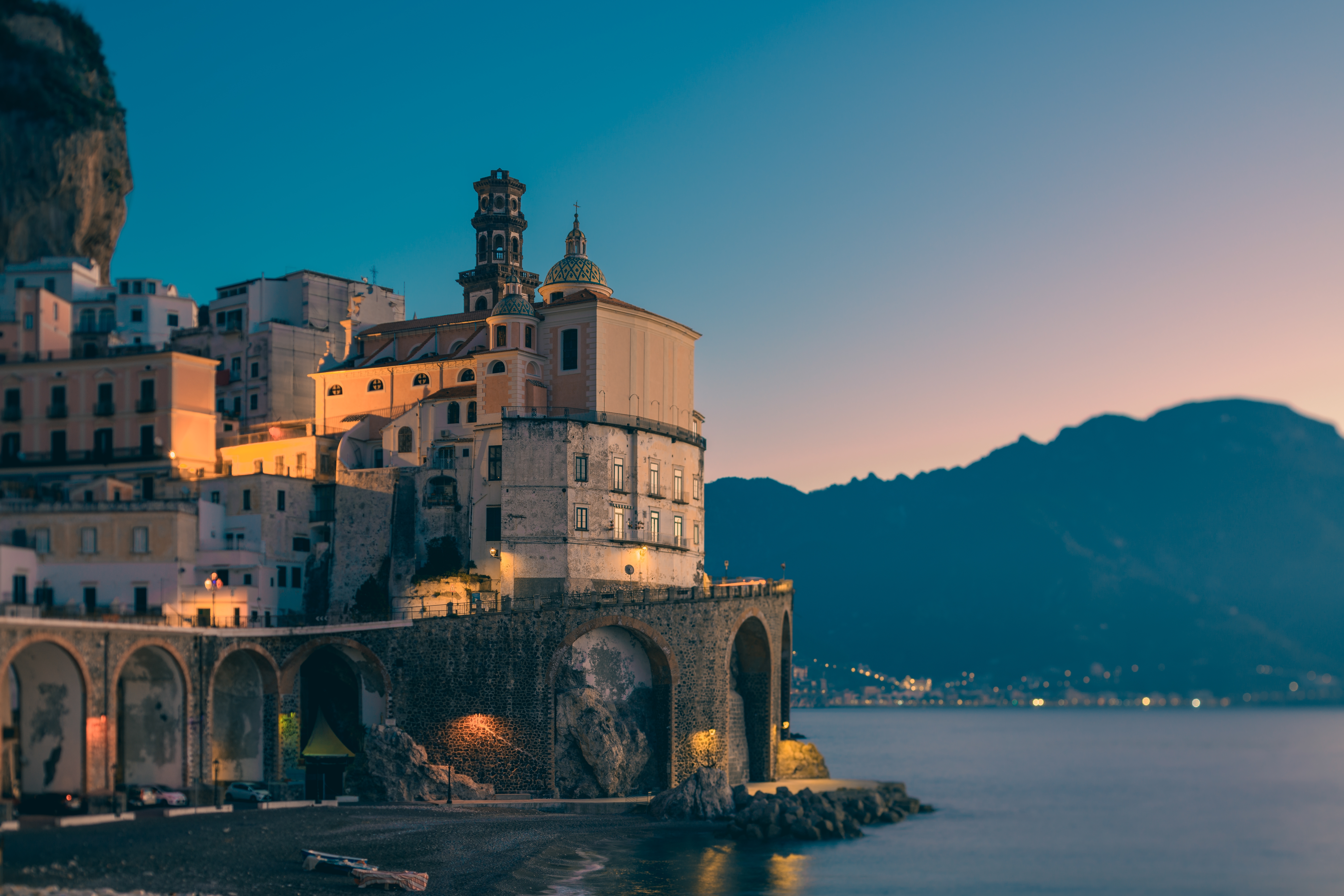 Den smukke kystby Atrani på Amalfikysten i Italien ved aftenstide med oplyst katedral og bjerge i horisonten