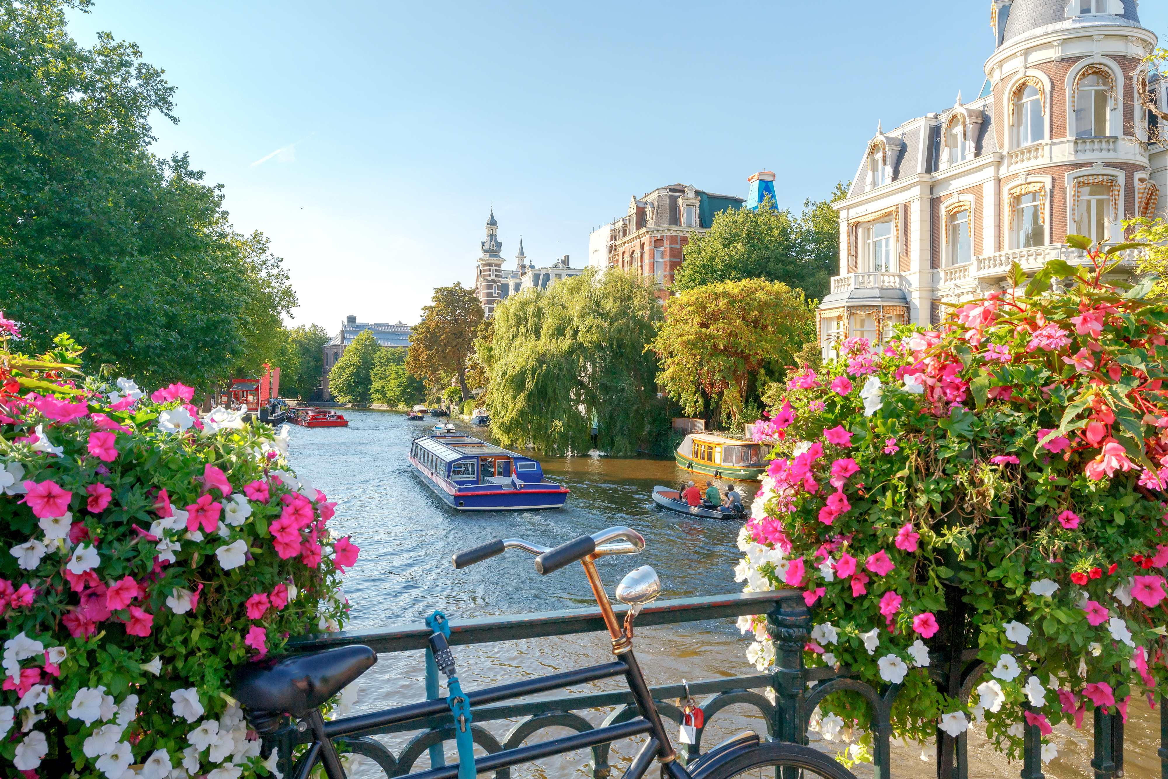 Stemningsfuld kanal i Amsterdams gamle bydel med karakteristiske smalle huse og perfekte vandspejlinger under blå himmel