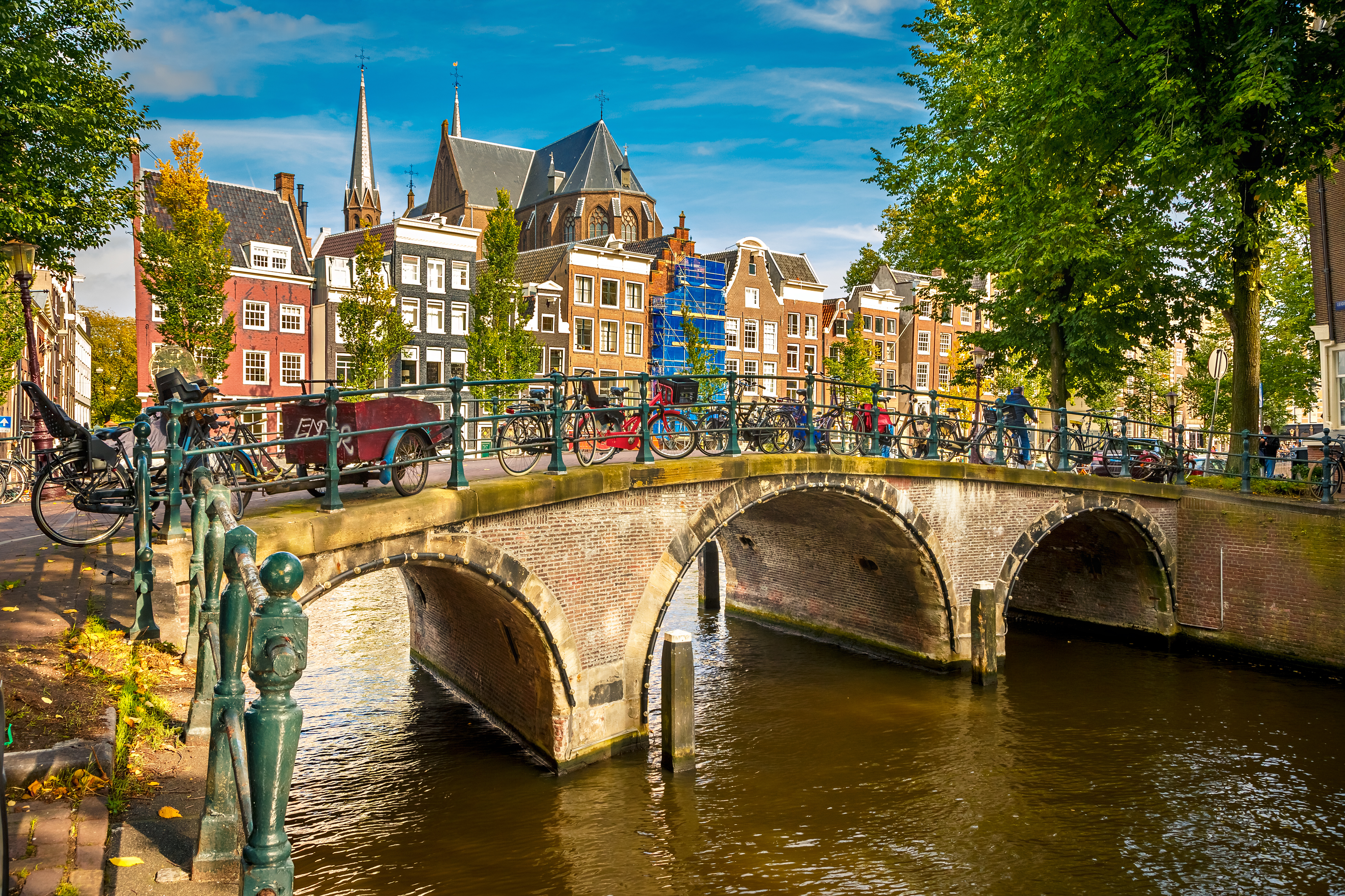 Malerisk kanalscene fra Prinsengracht i Amsterdam med stenbro, cykler og traditionelle hollandske huse i solskinsvejr