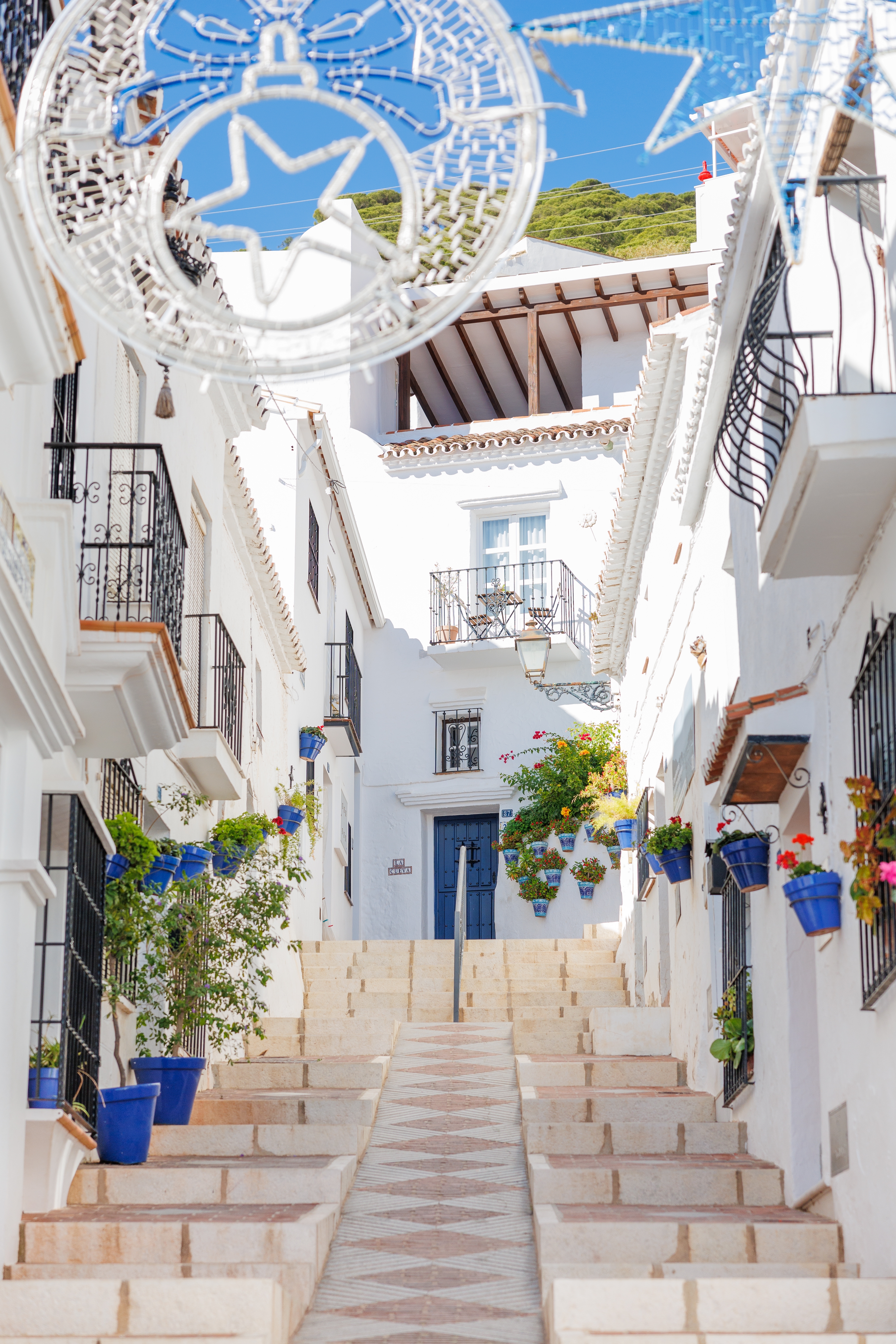 Hyggelig gade i den traditionelle andalusiske landsby Mijas Pueblo med hvidkalkede huse og blå blomsterpotter i Spanien