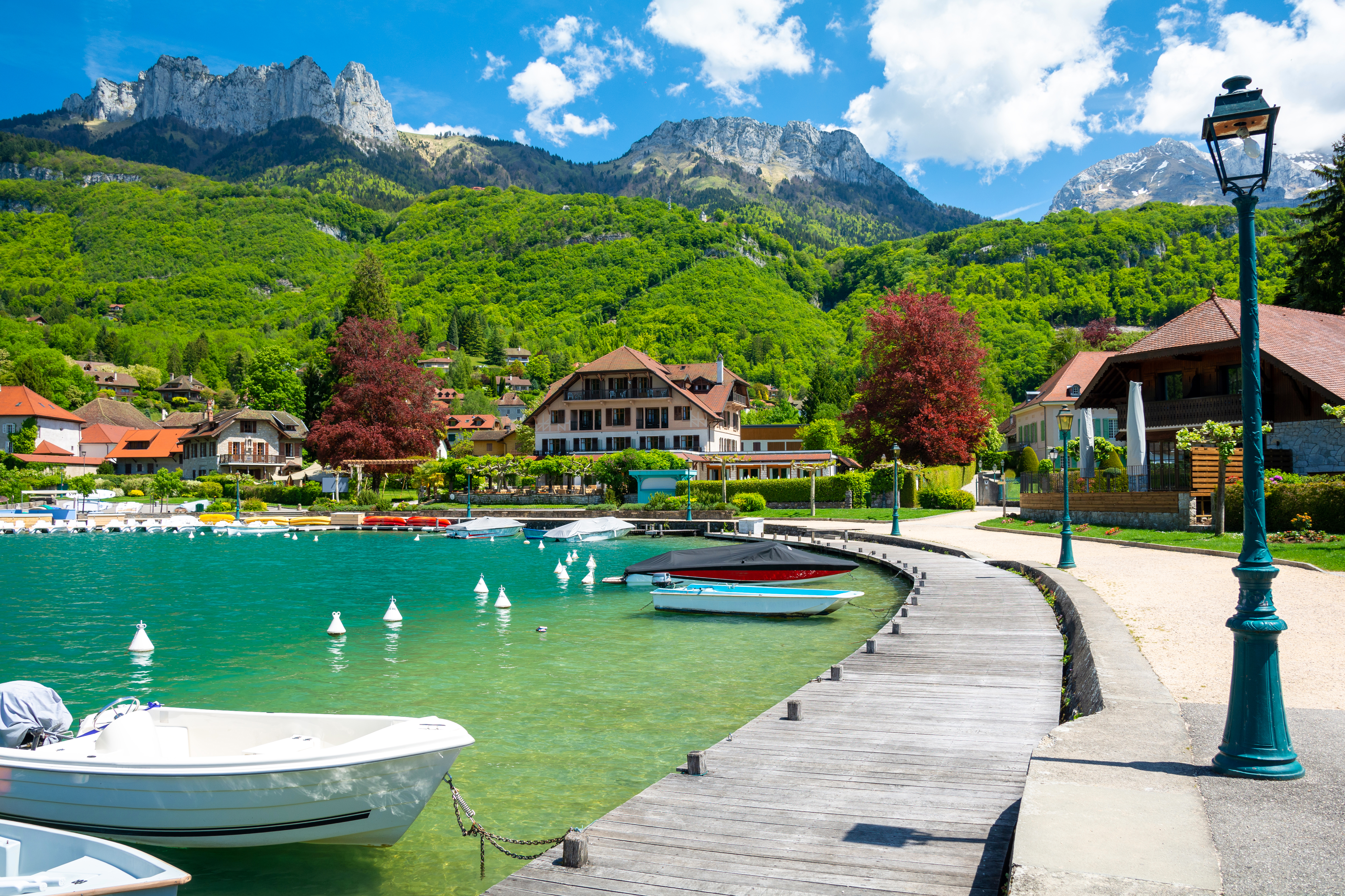 Malerisk fransk alpedestination ved Annecy-søen med farverige både, traditionelle huse og imponerende bjergkæde
