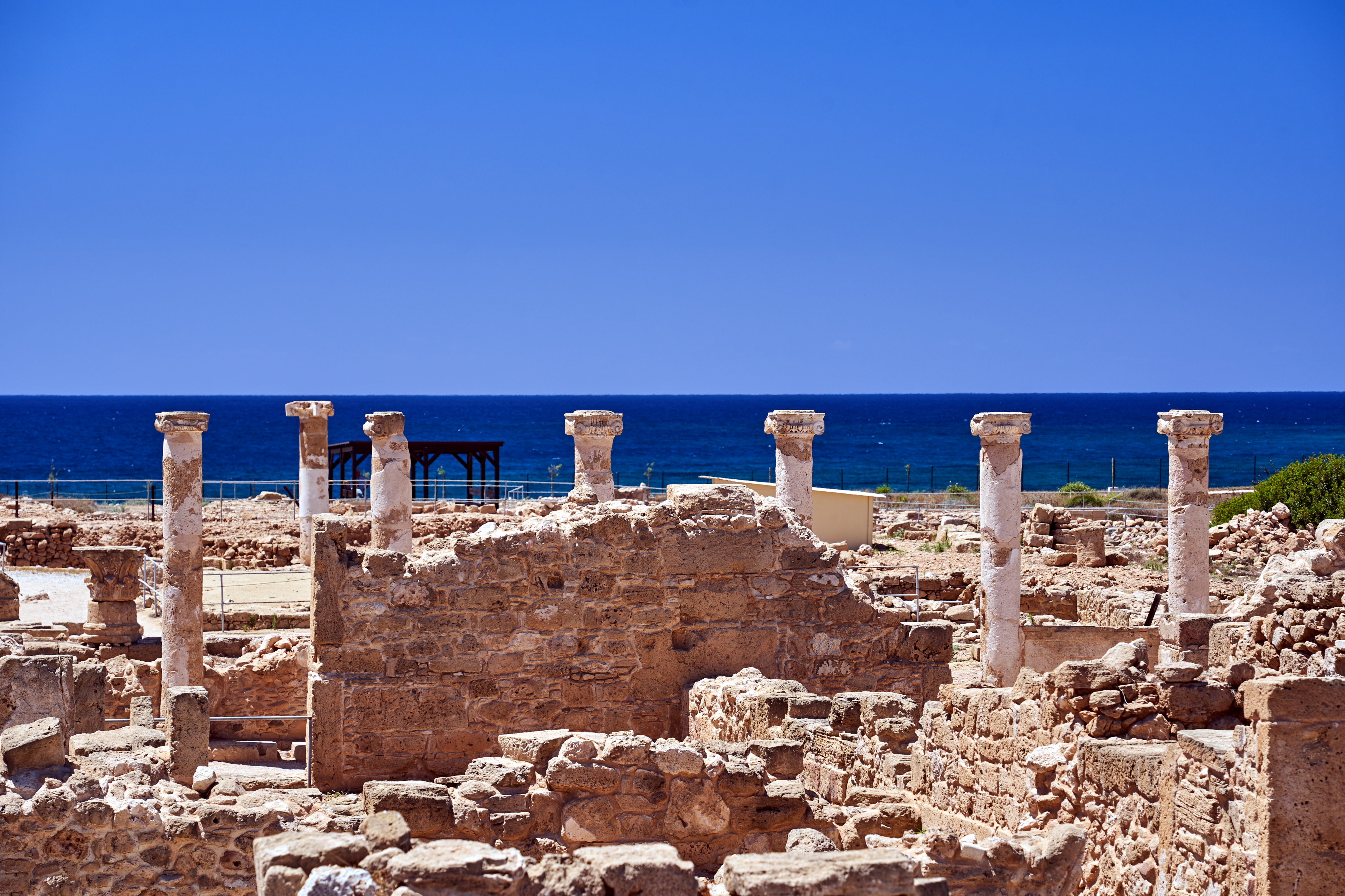 Smukke antikke søjler og stenruiner i Paphos arkæologiske park på Cypern med det turkisblå Middelhav bagved
