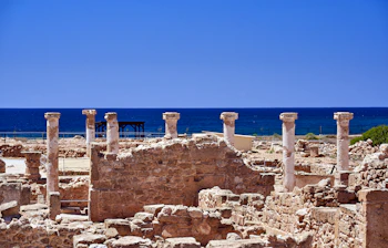 Smukke antikke søjler og stenruiner i Paphos arkæologiske park på Cypern med det turkisblå Middelhav bagved