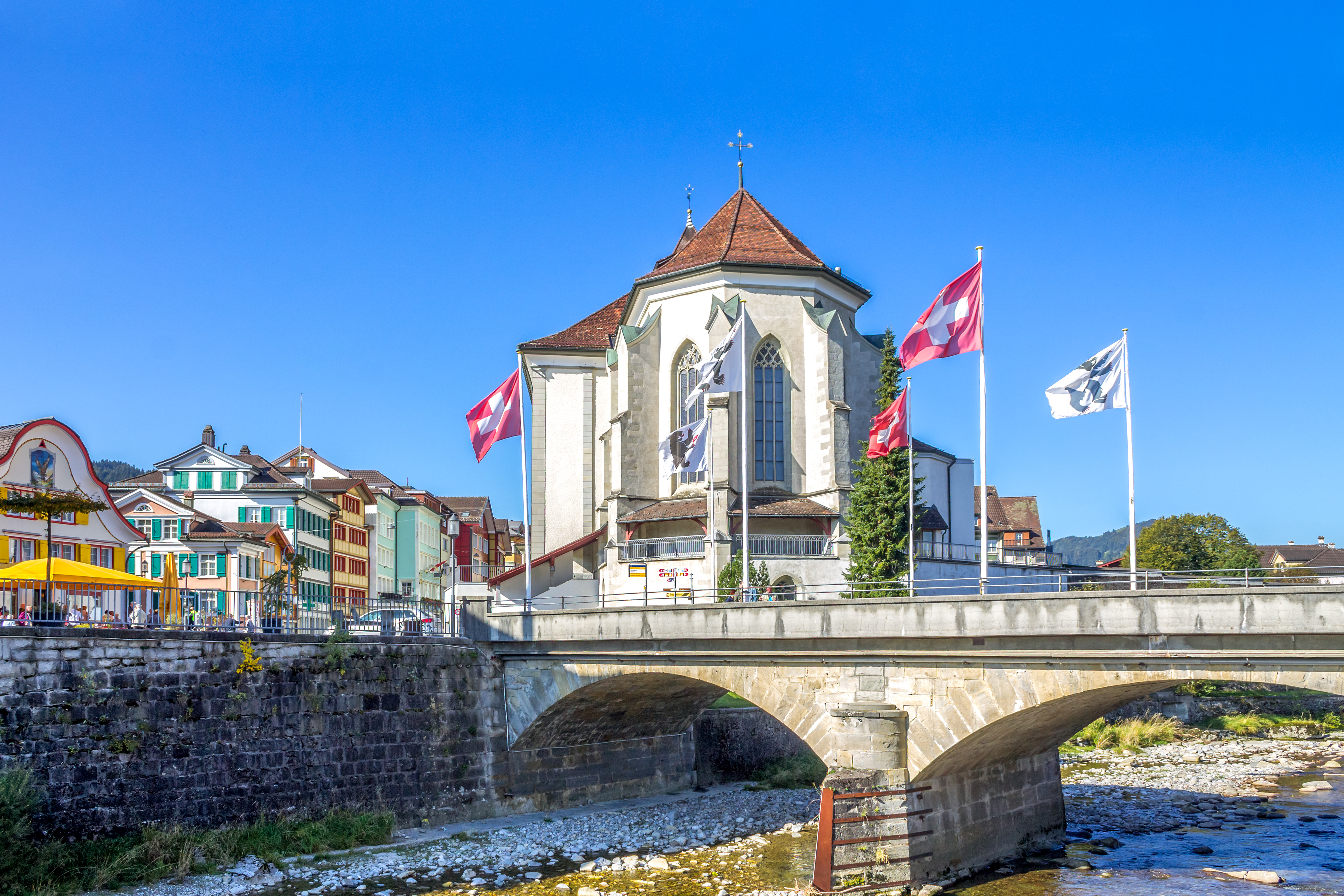 Historisk bykerne i Appenzell Schweiz med smukt kirketårn, stenbro over floden og traditionelle farverige huse