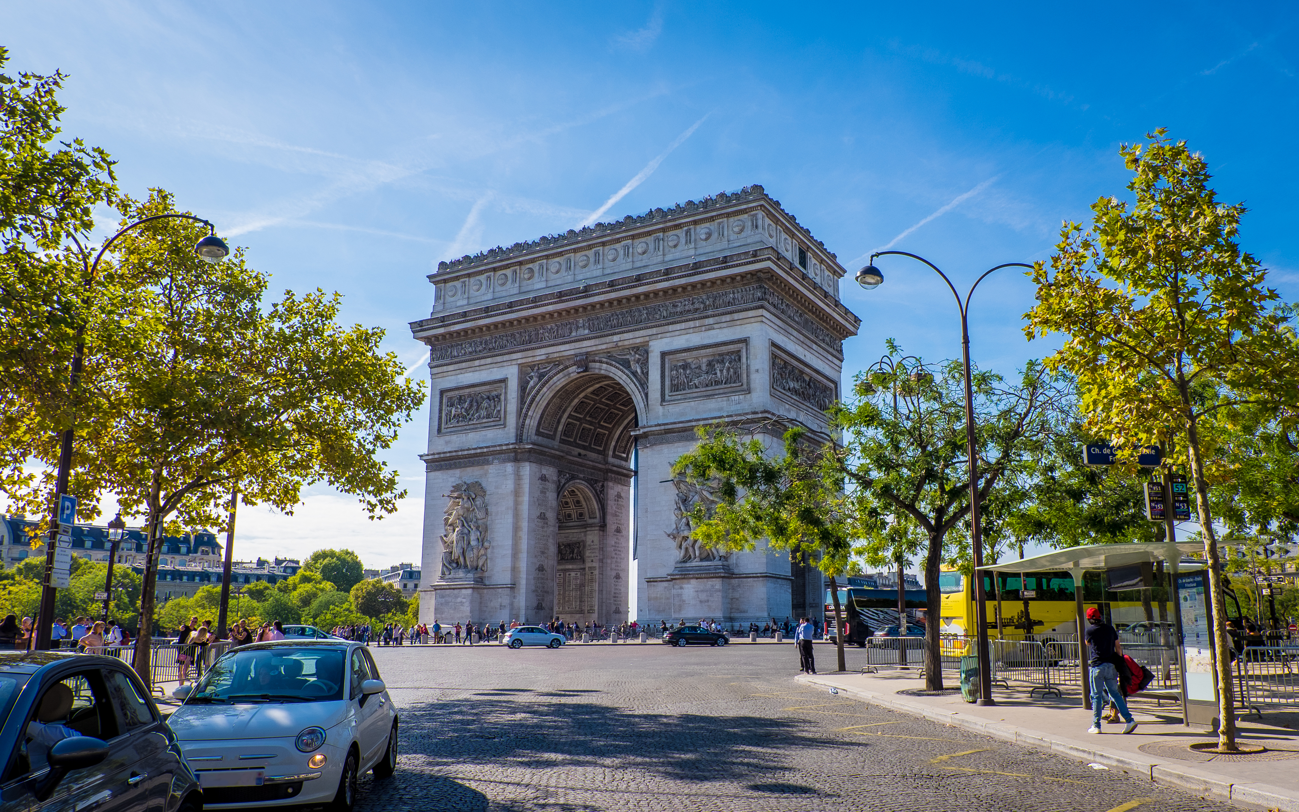 Arc de Triomphe i hjertet af Paris med travle gader og smukke træer under blå himmel