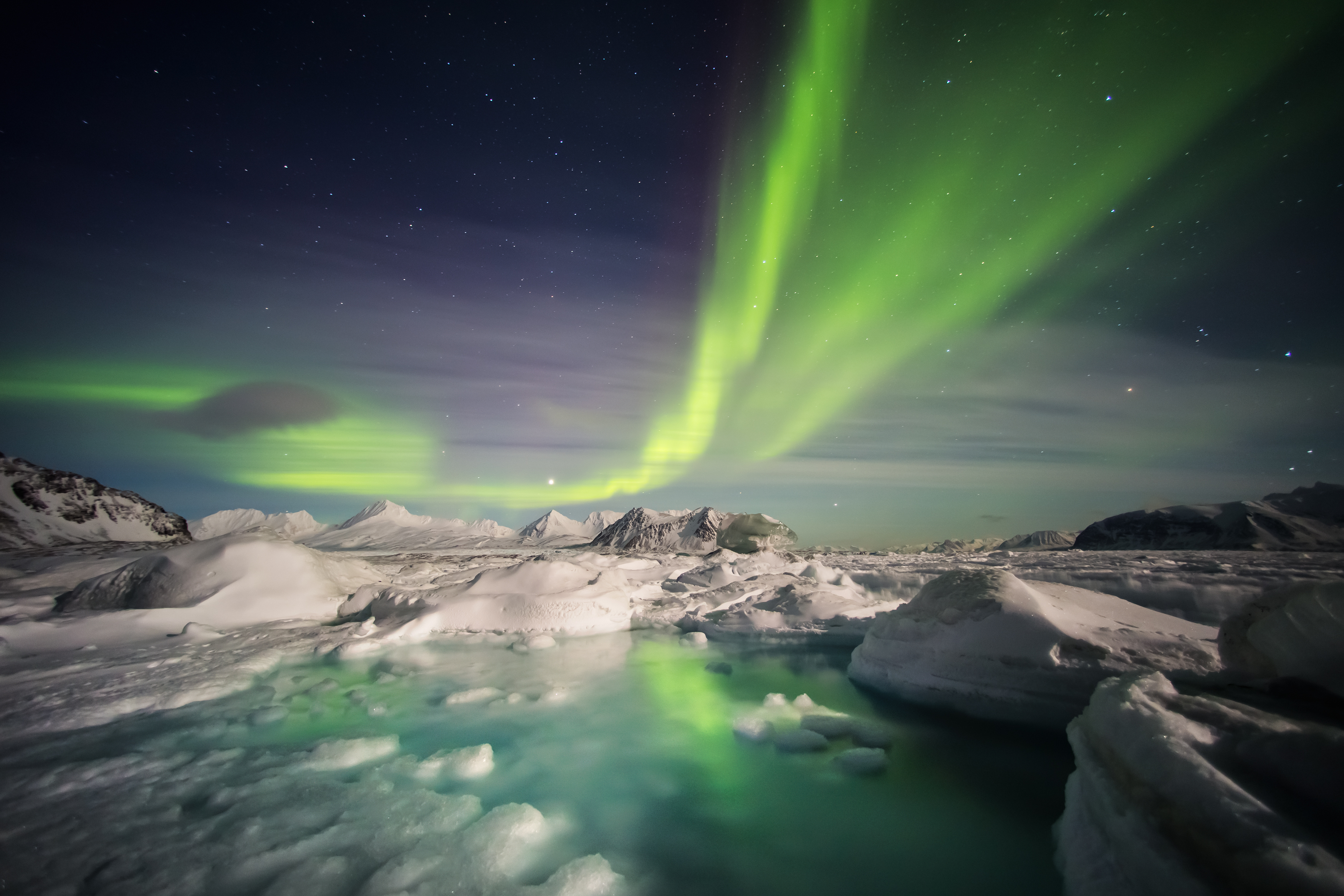 Fantastiske nordlys i grønne og violette toner over det snedækkede arktiske landskab ved Svalbard om vinteren
