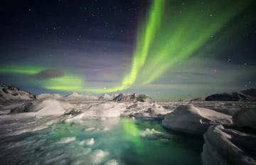 Fantastiske nordlys i grønne og violette toner over det snedækkede arktiske landskab ved Svalbard om vinteren