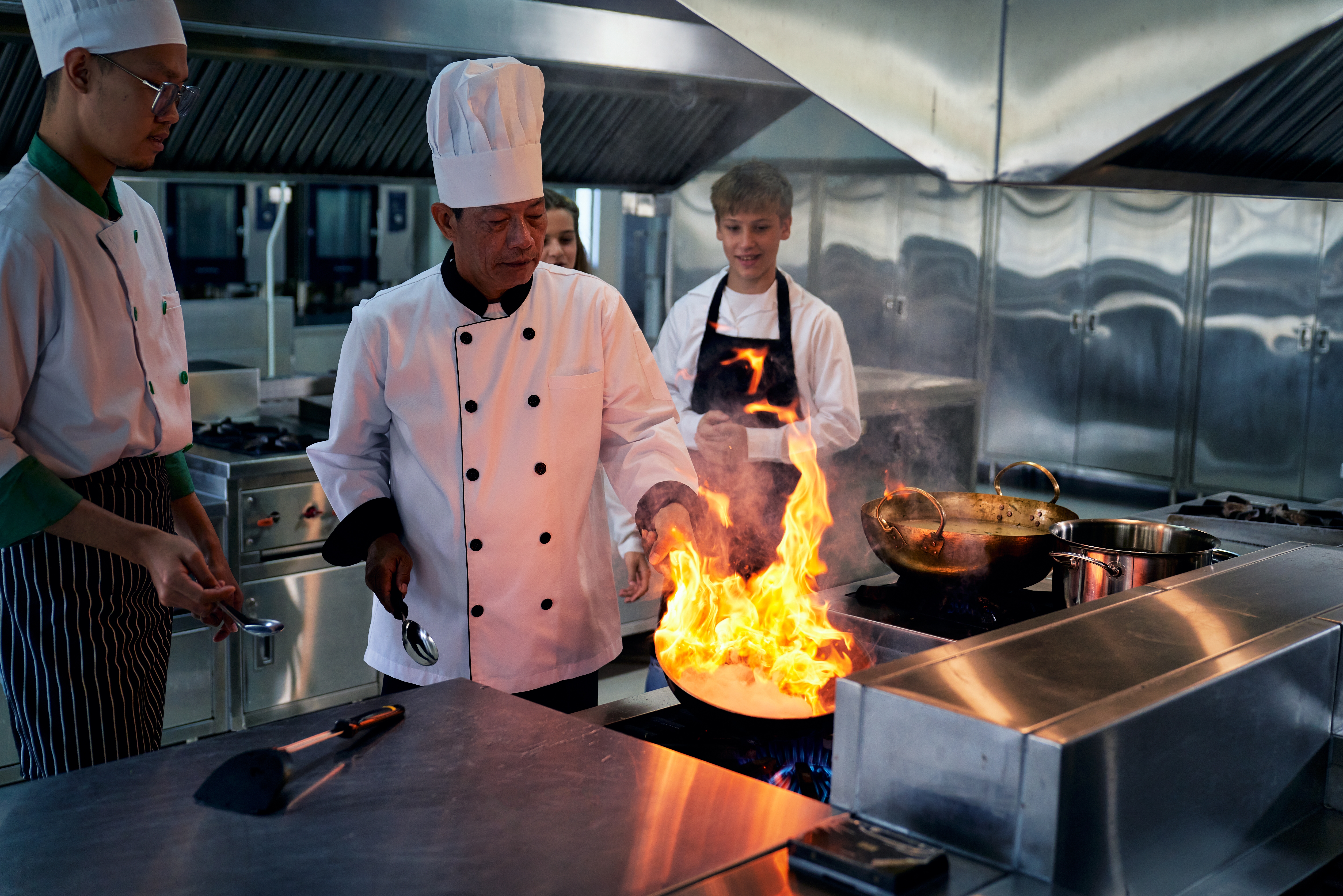 Erfaren asiatisk kok demonstrerer traditionel wok-madlavning med flammer for kokkeelever i professionelt køkken