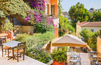 Idyllisk udendørs café i Plaka, Athen, med farverige bougainvillea-blomster, parasol og frodig beplantning på en solrig dag i Grækenland