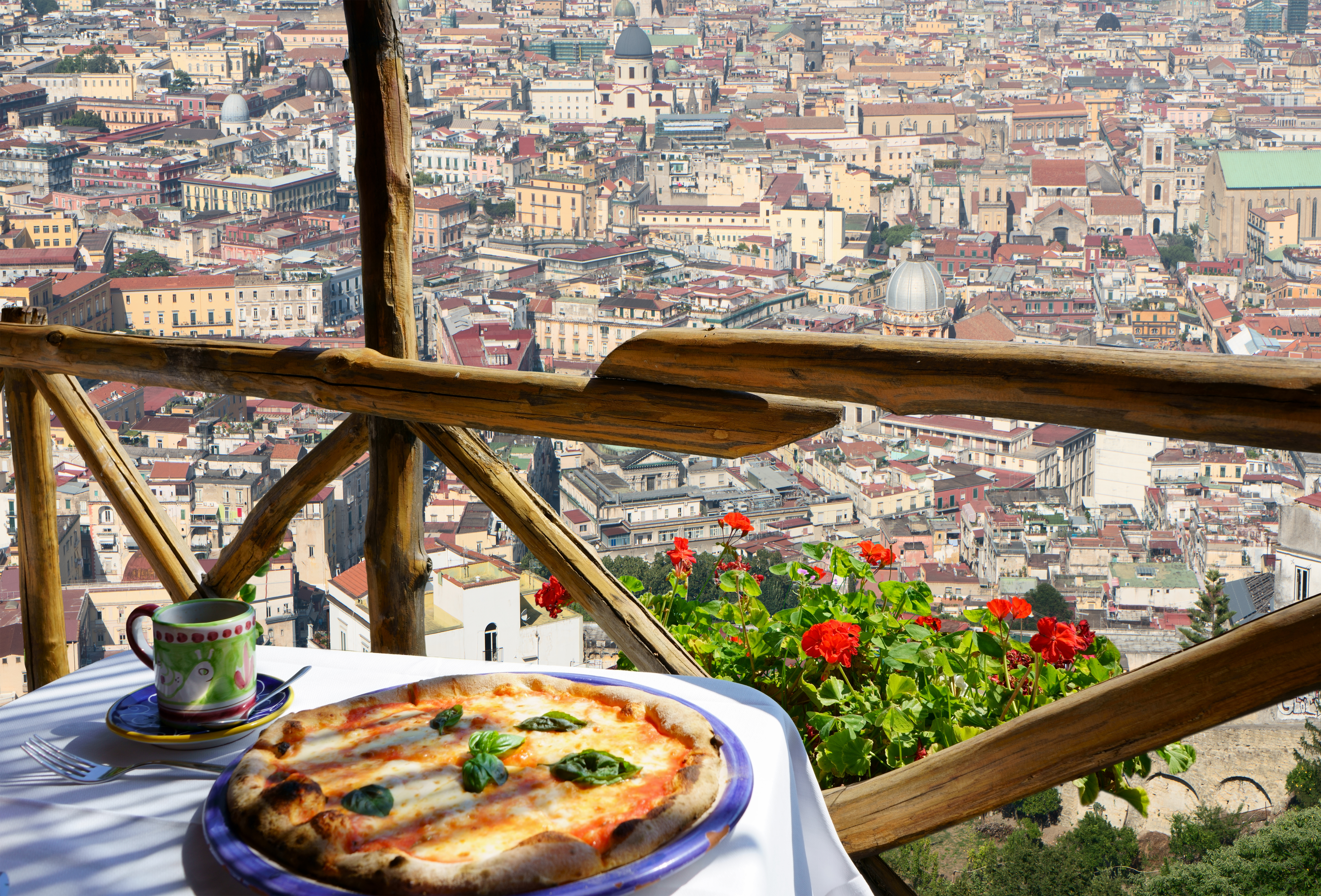 Ægte italiensk pizza Margherita nydes på bjergterrasse med storslået panorama over Napoli og røde blomster