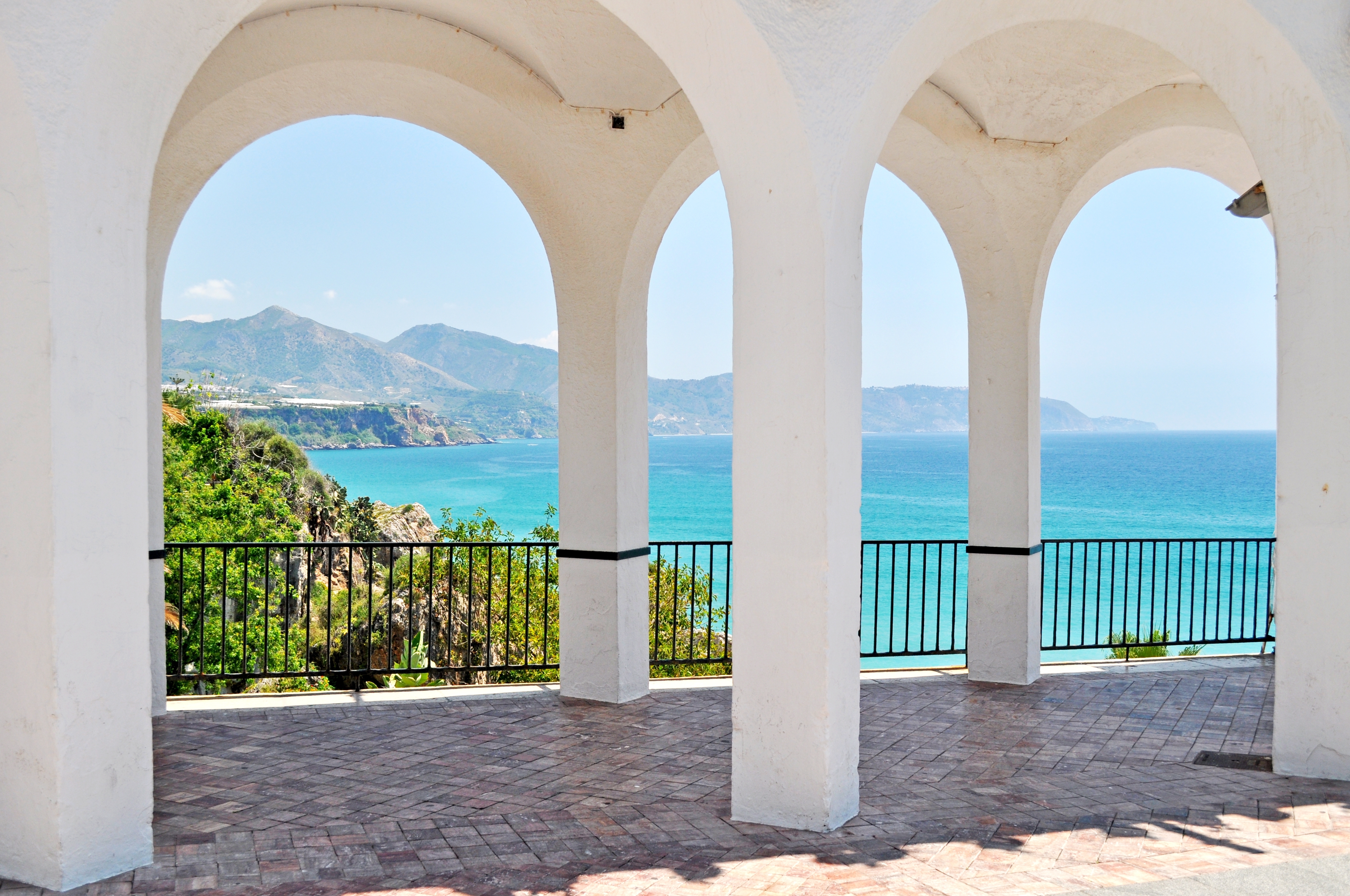 Fredelig udsigt fra Balcon de Europa i Nerja, Spanien, gennem elegante hvide stenbuer mod det turkisblå Middelhav og bjerglandskab