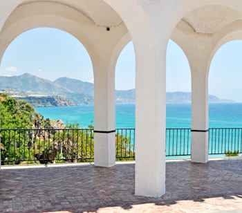 Fredelig udsigt fra Balcon de Europa i Nerja, Spanien, gennem elegante hvide stenbuer mod det turkisblå Middelhav og bjerglandskab