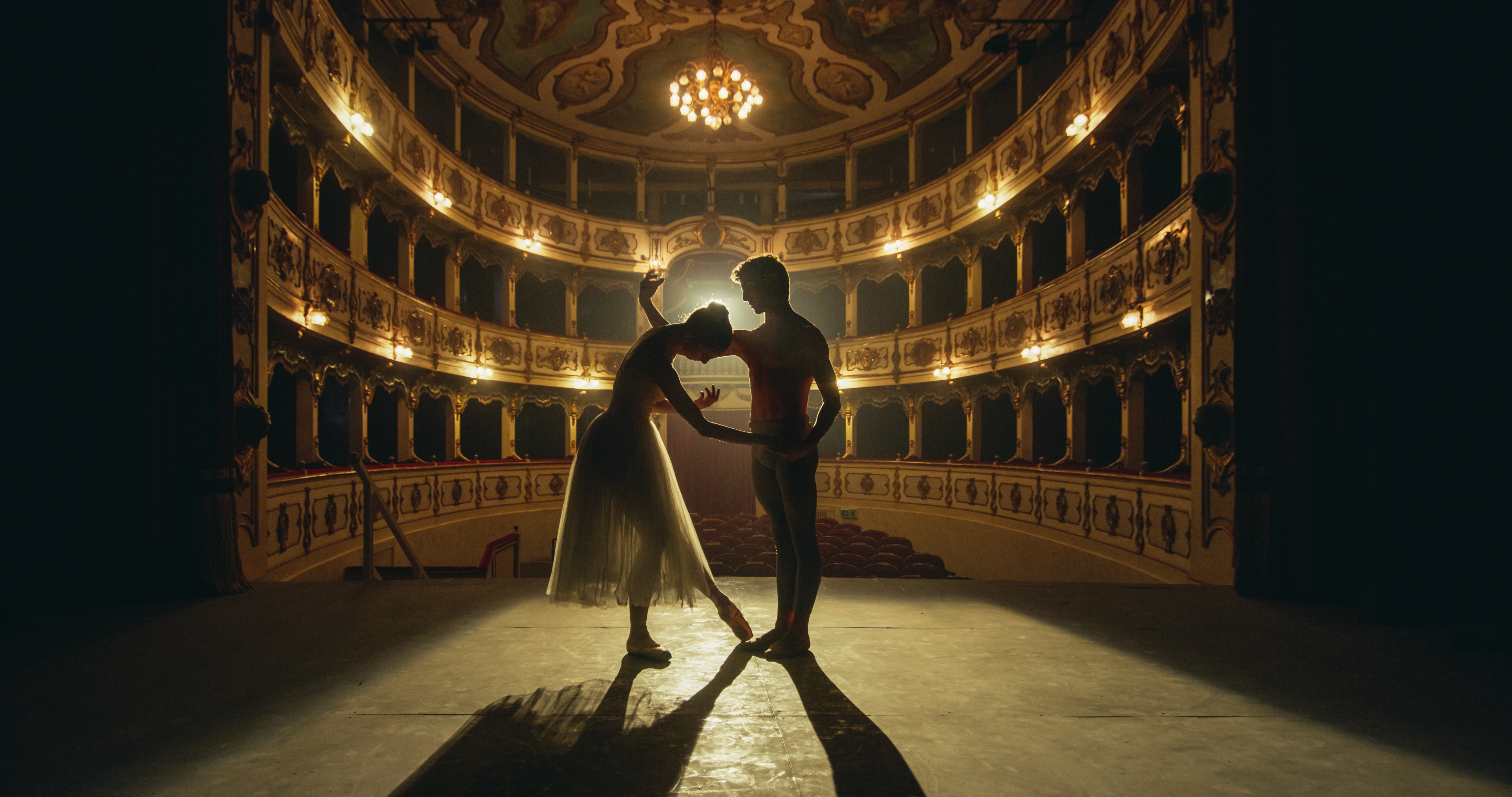 To ballettdansere i smuk silhuet udfører klassisk ballet på en dramatisk oplyst scene i et historisk pragtfuldt teater