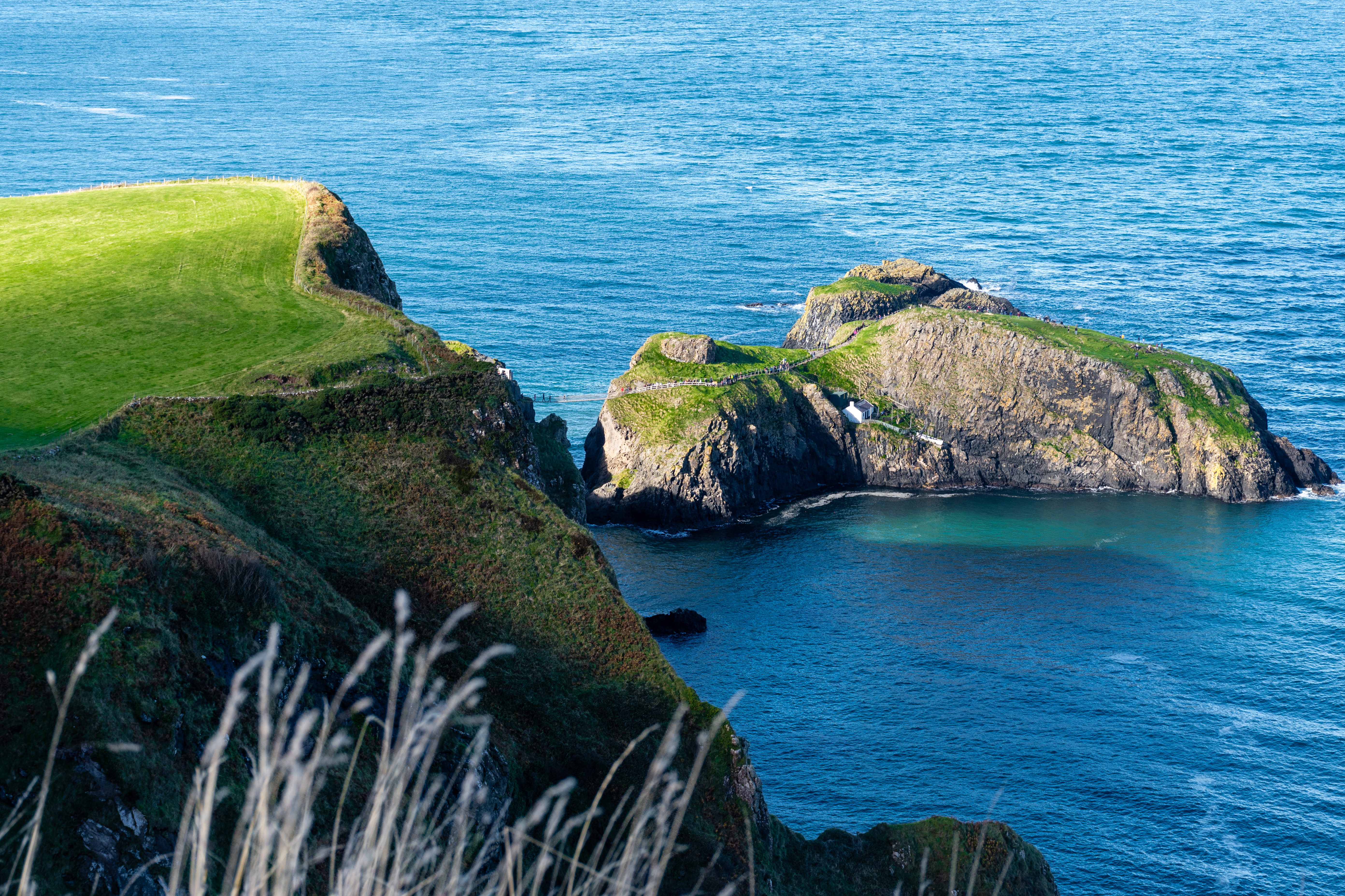 Imponerende Carrick-a-Rede hængebro nær Ballycastle i Nordirland med panoramaudsigt over det krystalklare hav og de omkringliggende øer