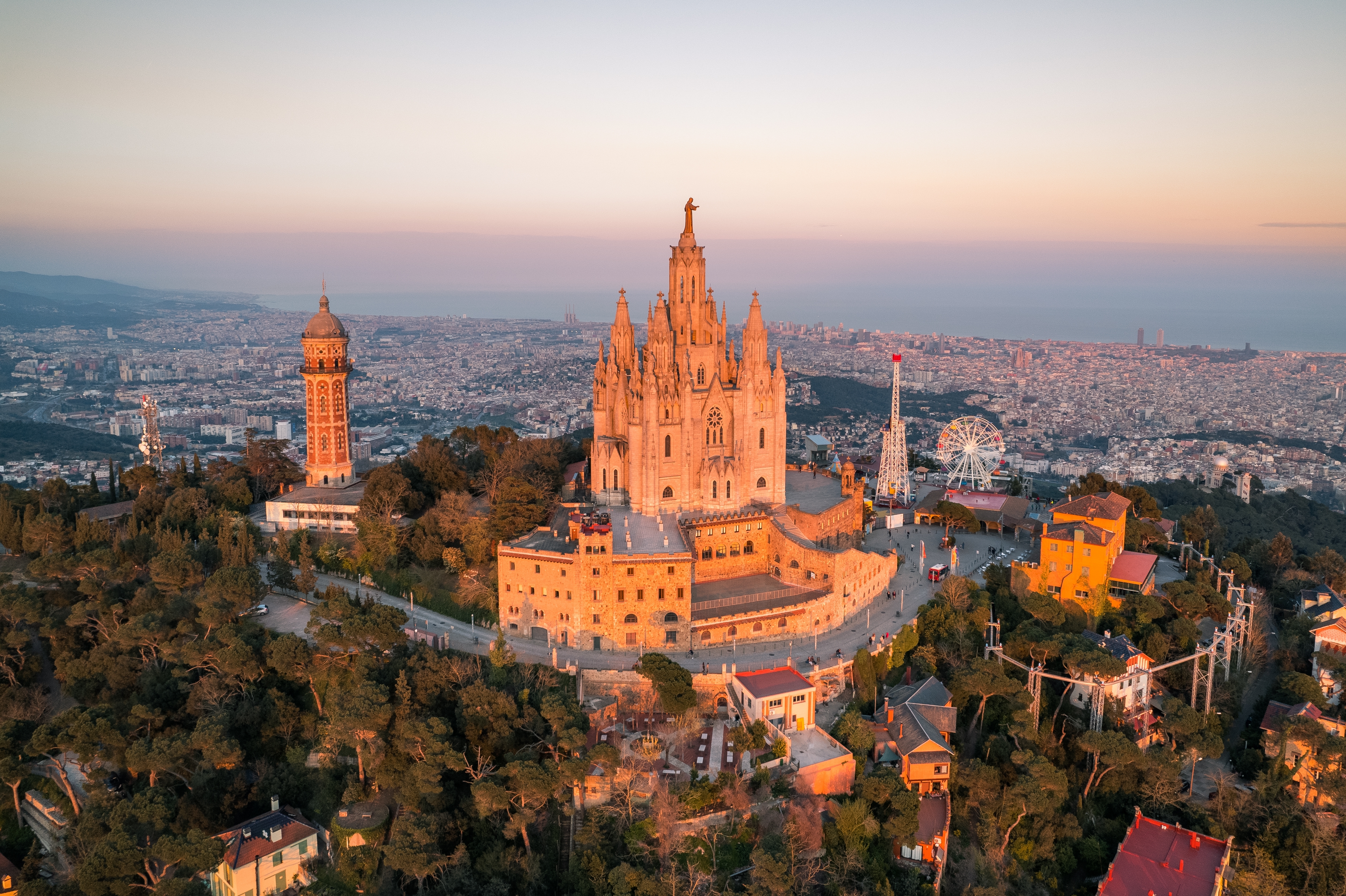 Flot luftfoto af den historiske Tibidabo-kirke i Barcelona ved solnedgang med udsigt over den spanske storby og Middelhavet