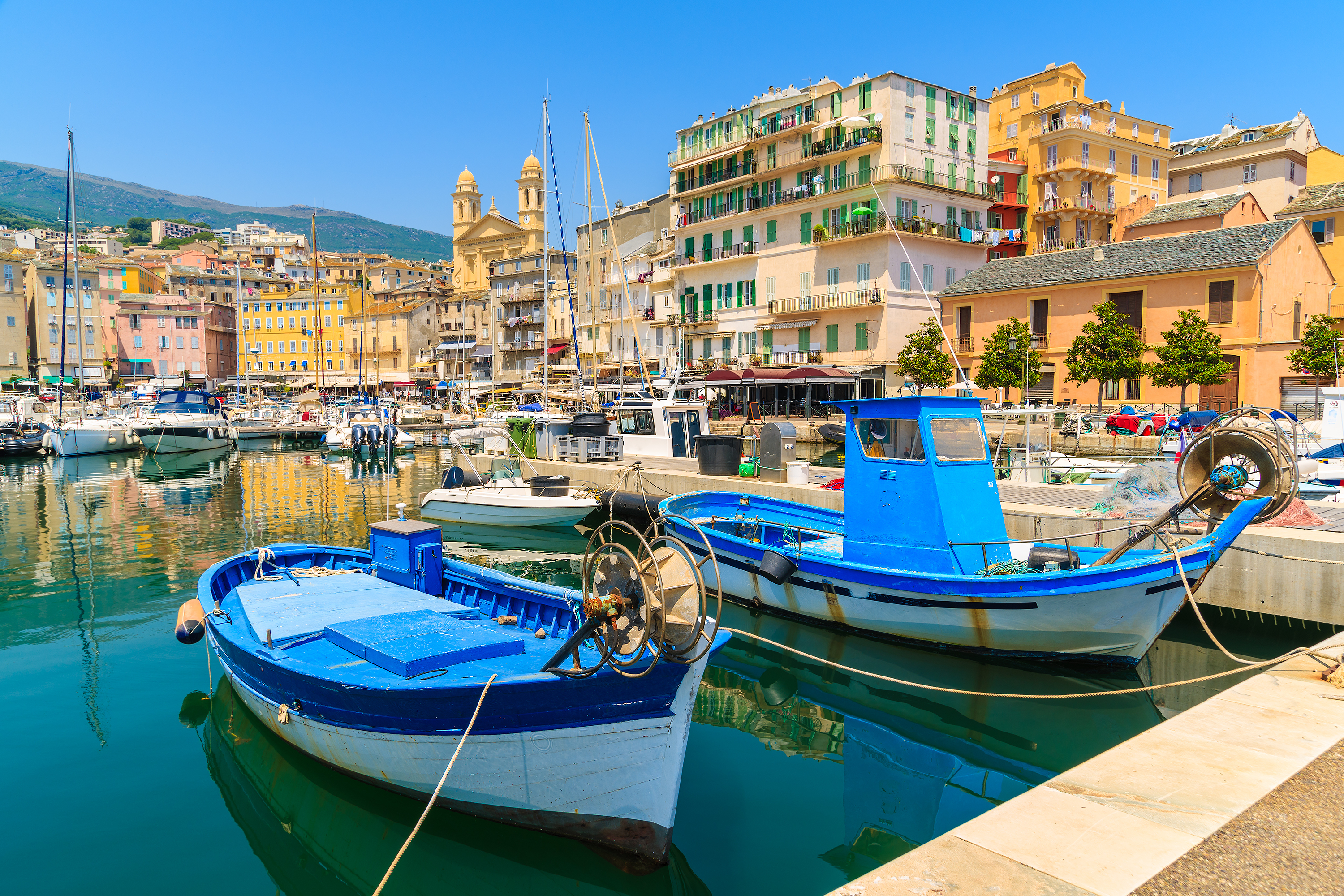 Stemningsfuld udsigt over den pittoreske havn i Bastia på Korsika, hvor traditionelle fiskerbåde ligger fortøjet ved kajen med den historiske bymidte som smuk kulisse