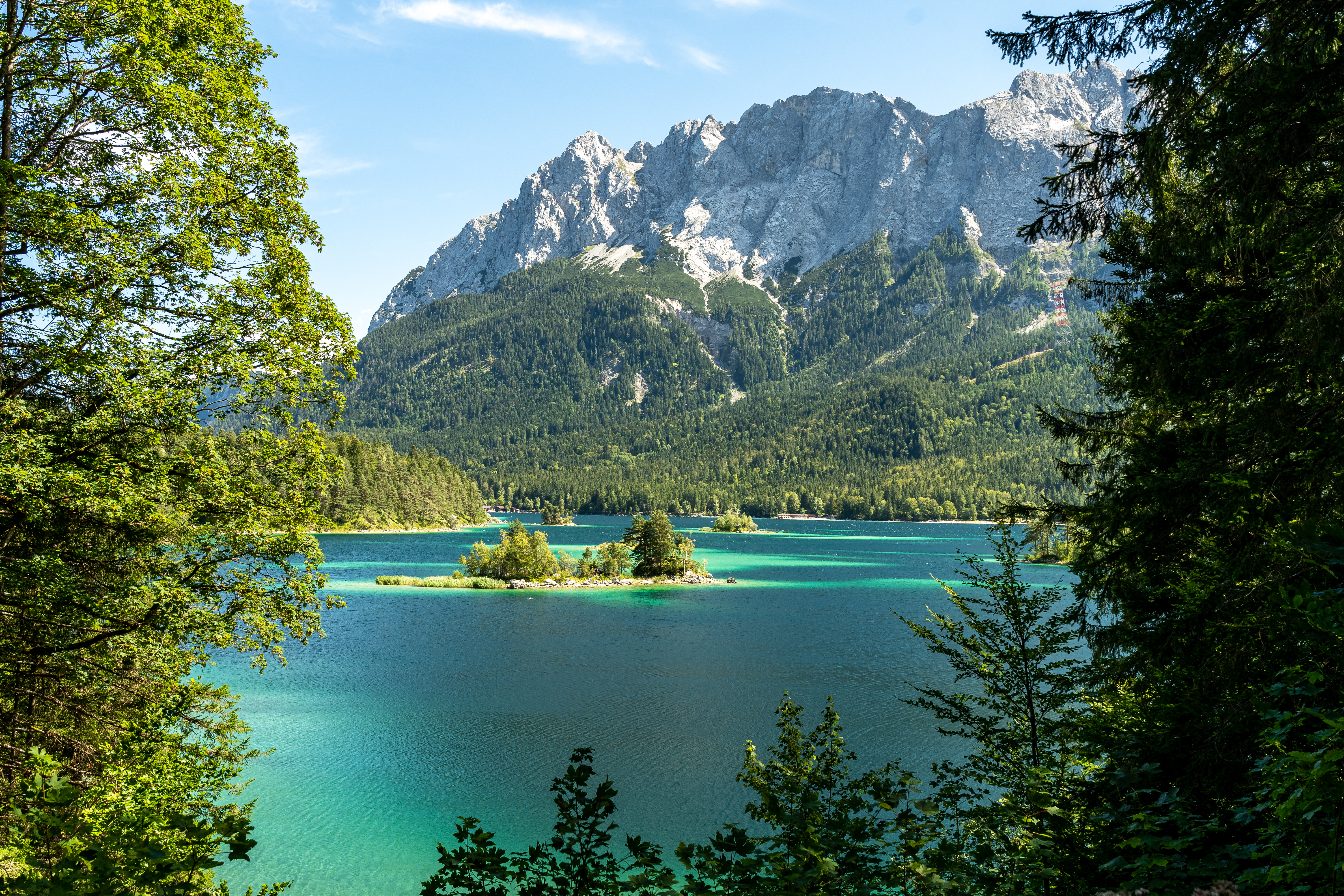 Idyllisk sommerbillede af det turkisblå Eibsee med skovklædte bredder og Zugspitze bjerget i baggrunden, Bayern