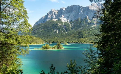 Idyllisk sommerbillede af det turkisblå Eibsee med skovklædte bredder og Zugspitze bjerget i baggrunden, Bayern