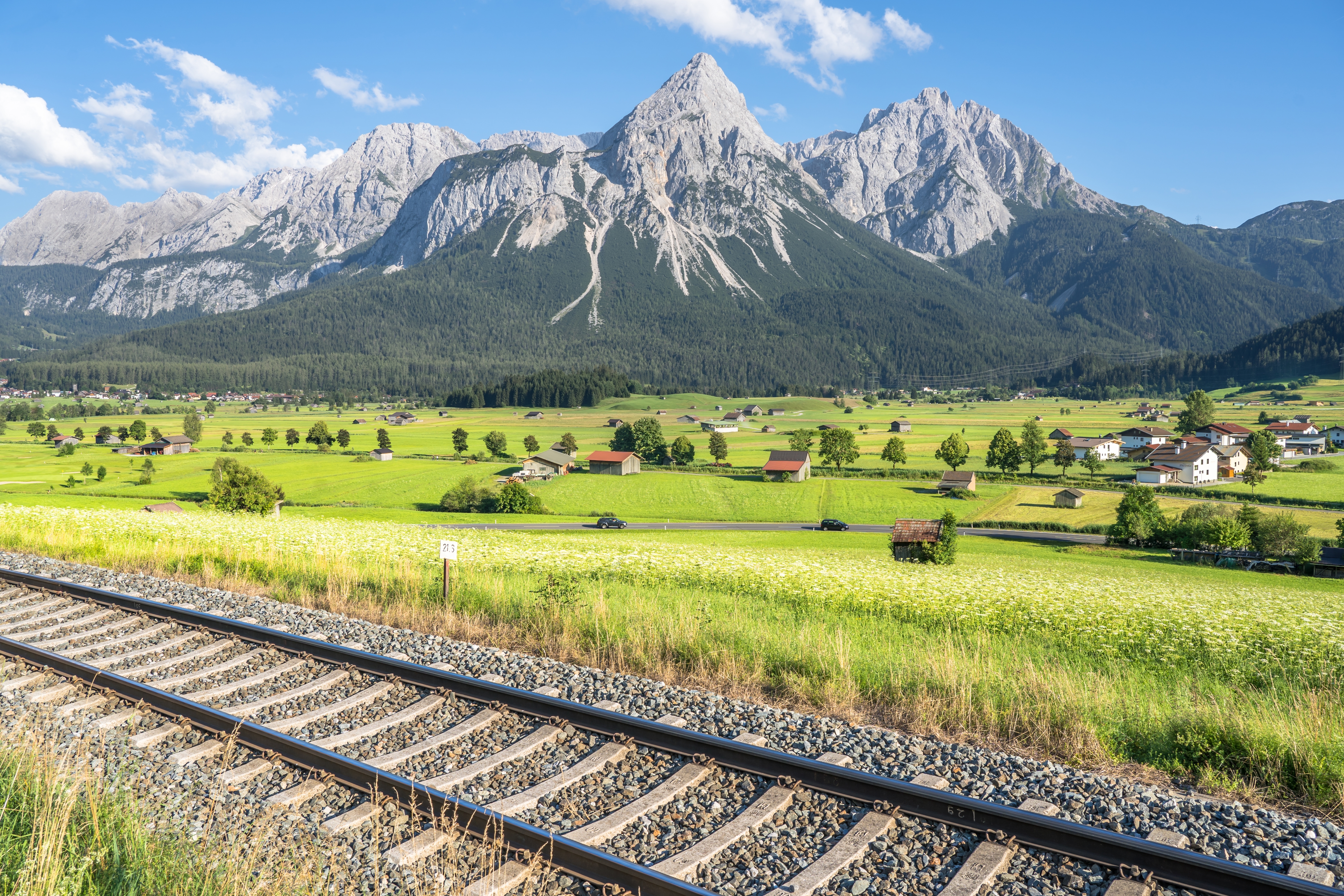 Jernbanelinje i forgrunden med grønne sommerage og den spektakulære Zugspitze i baggrunden ved Ehrwald i de bayerske alper, Tyskland