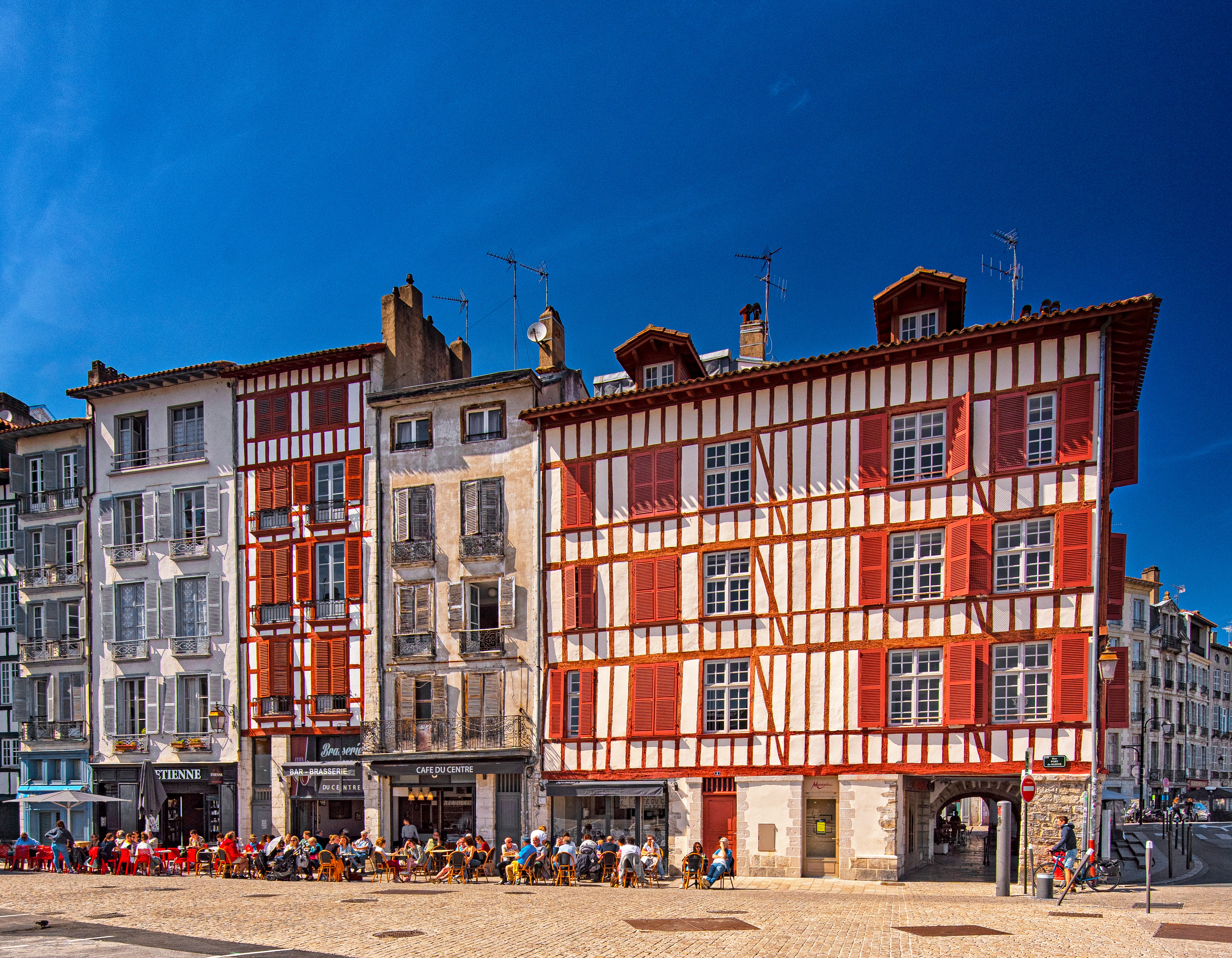 Historiske bindingsværksbygninger med røde skodder og udendørs caféer på Place de la Liberté i Bayonne, Frankrig