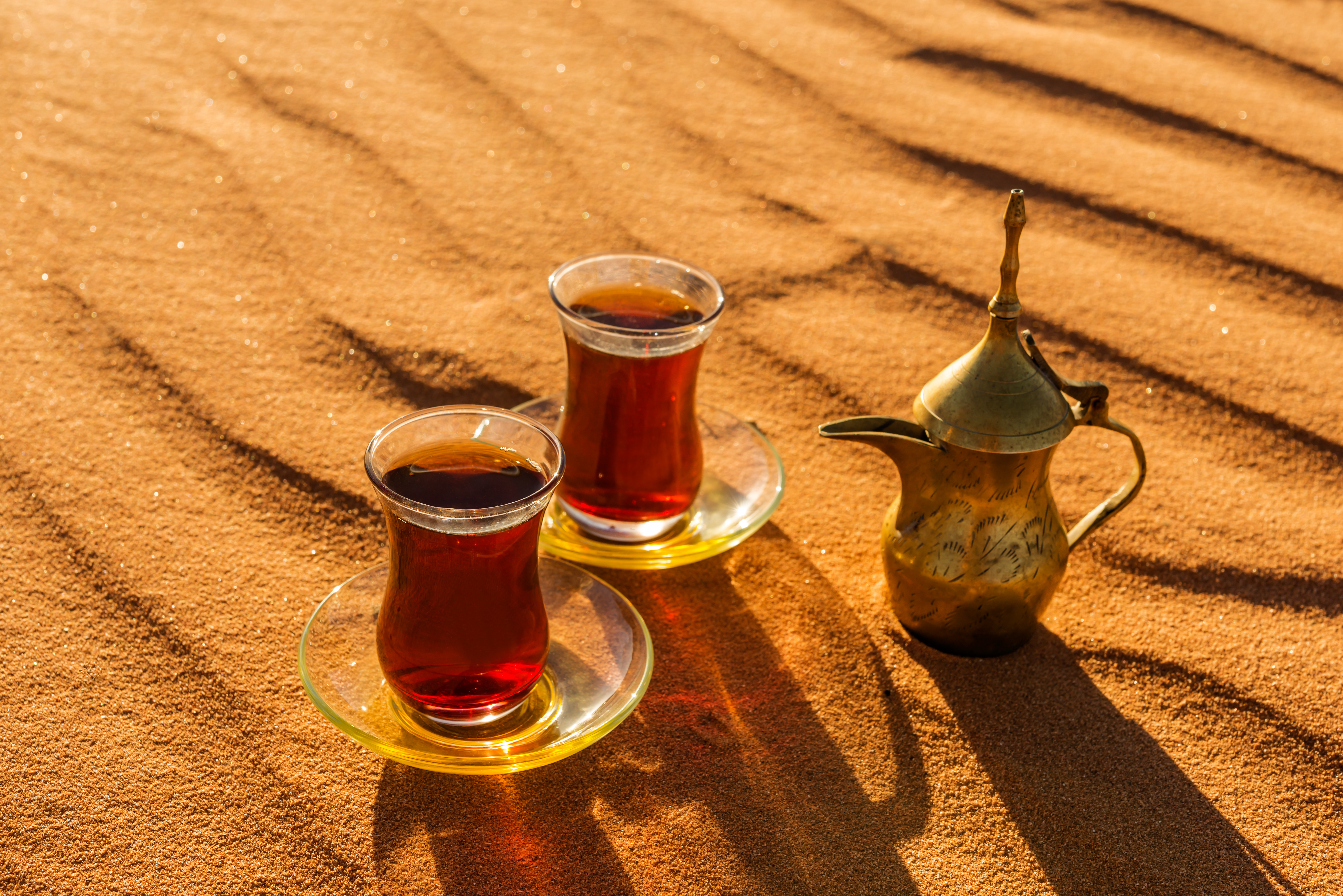 Beduin-inspireret te-ceremoni med ornamenterede glas og kande på sanddynerne i Qatar ved solnedgangstid