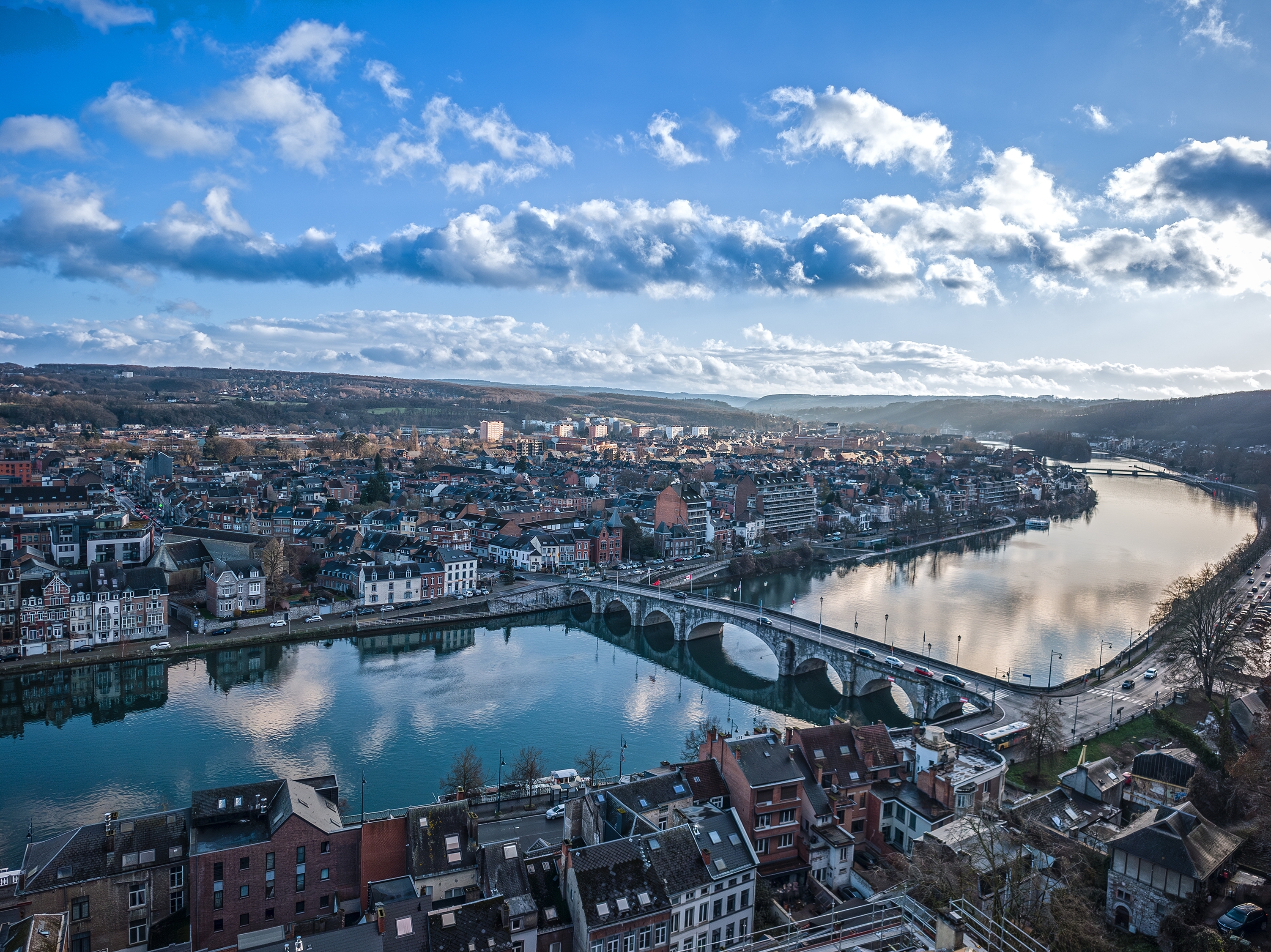 Vidtstrakt udsigt over Namur i Belgien med den vindende Meuse-flod, historisk arkitektur og en smuk bro under en delvist skyet himmel