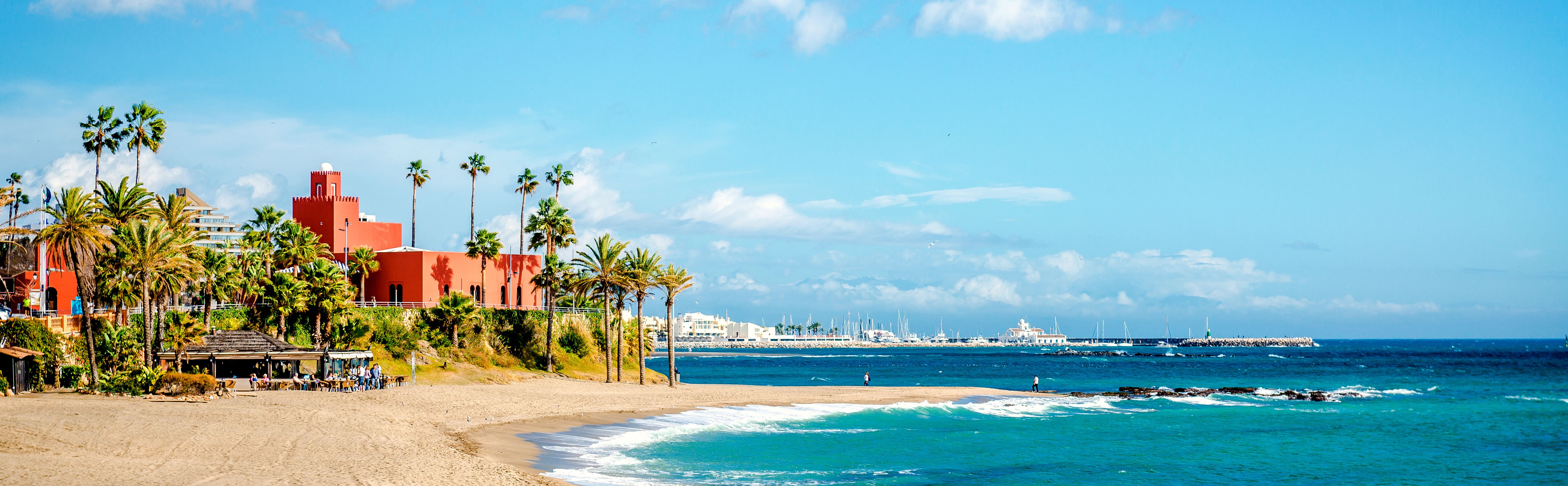 Indbydende strandudsigt i Benalmadena ved Malaga, Costa del Sol, med bølger der skyller ind mod den gyldne sand, palmer og det smukke turkise middelhav