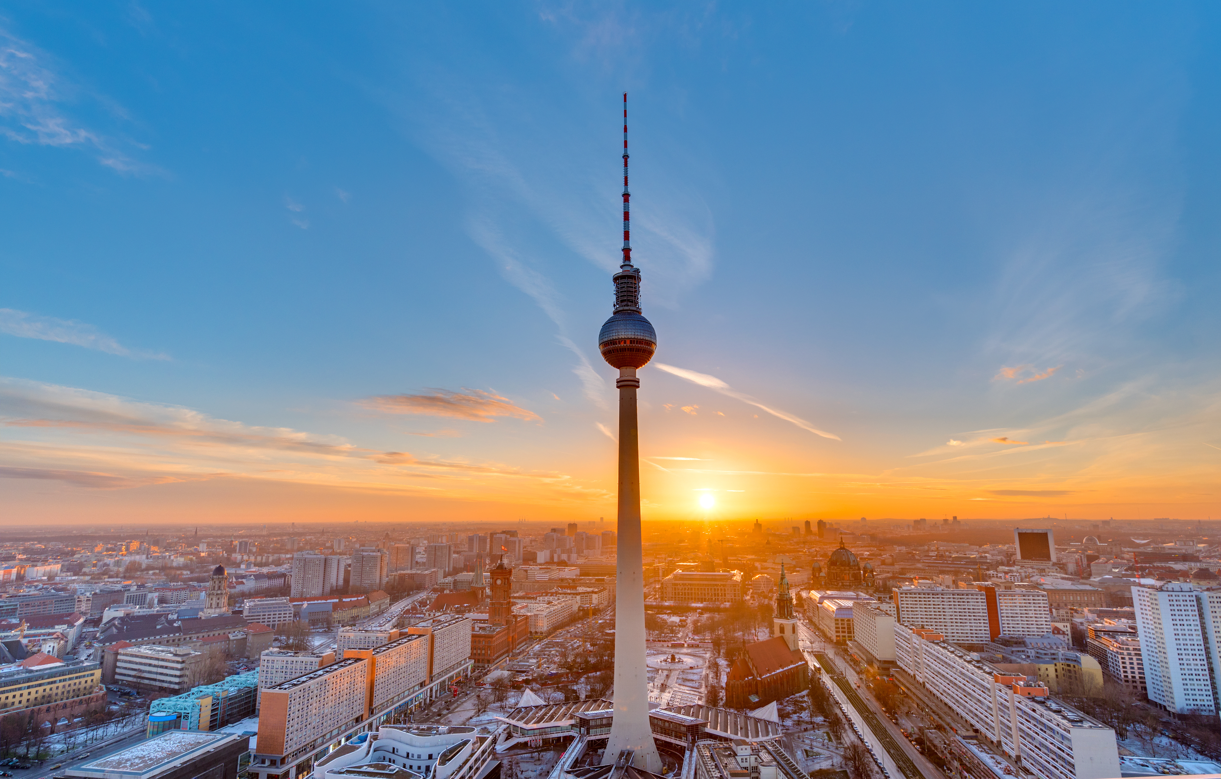 Imponerende udsigt over Berlin og Fernsehturm TV-tårnet ved Alexanderplatz under en spektakulær solnedgang med orange og blå himmel