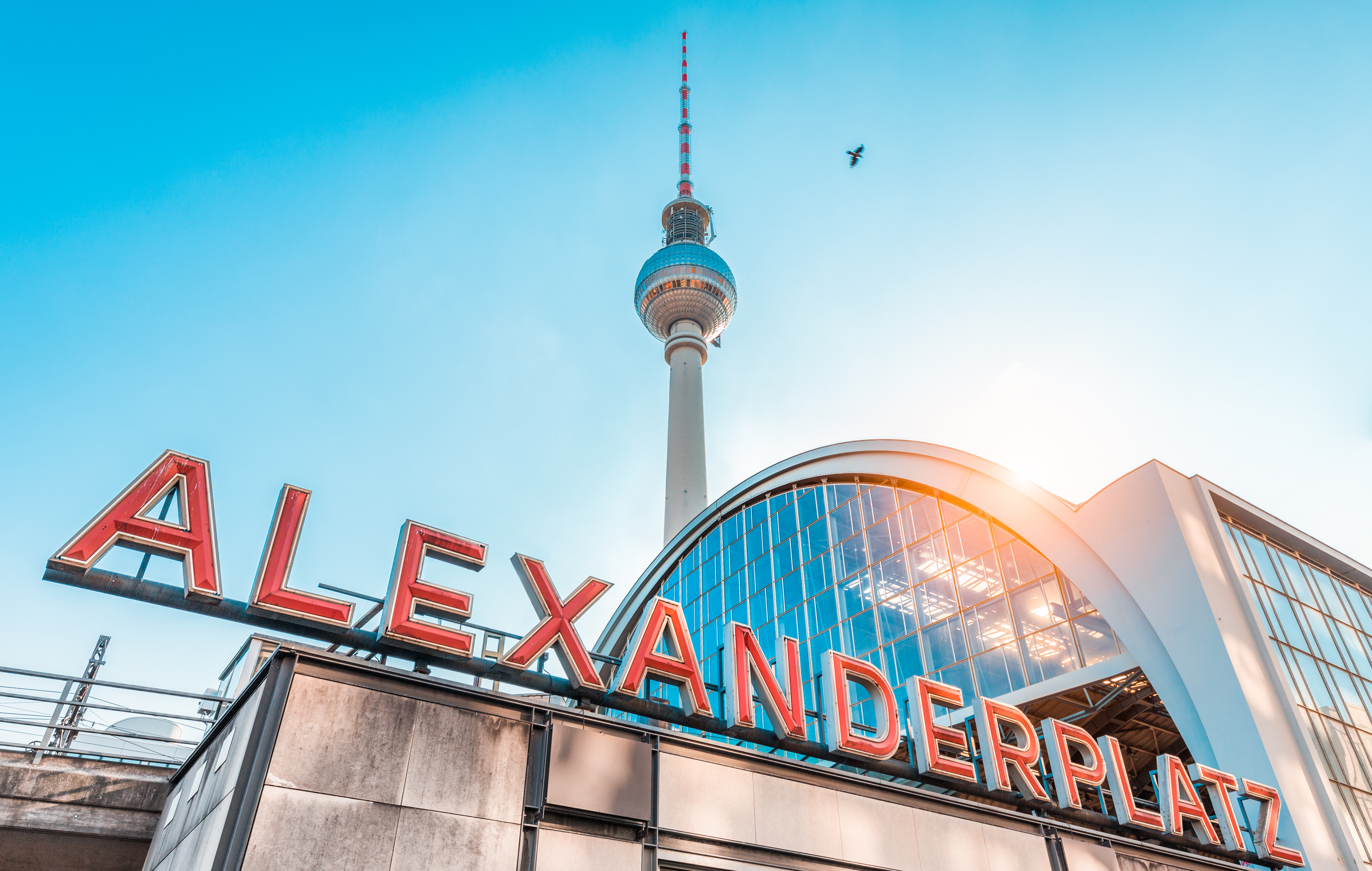 Alexanderplatz stationsskilt i Berlin med det høje TV-tårn og blå himmel i baggrunden