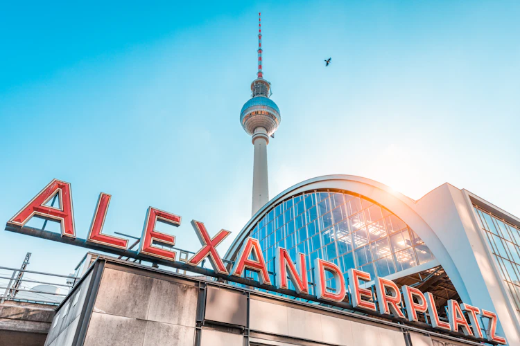 Alexanderplatz stationsskilt i Berlin med det høje TV-tårn og blå himmel i baggrunden