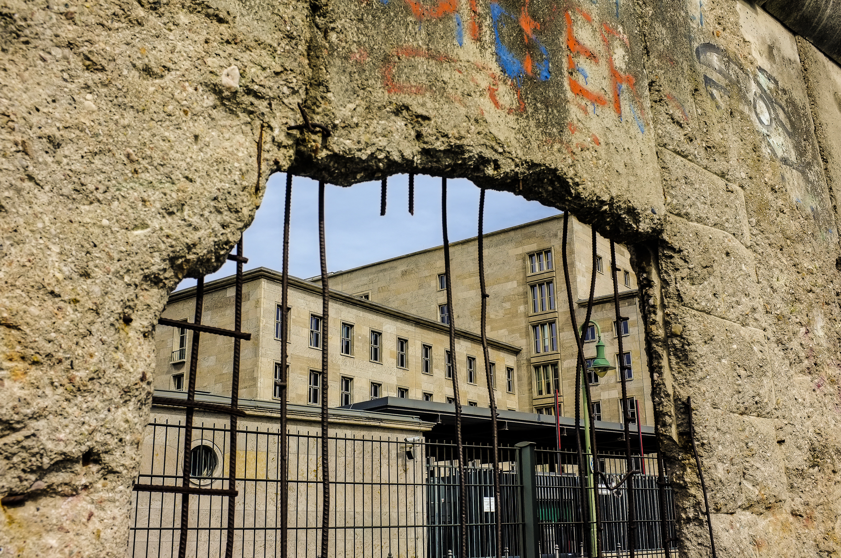 Berlinmurens betonbarriere med graffiti og historisk bygning gennem hul