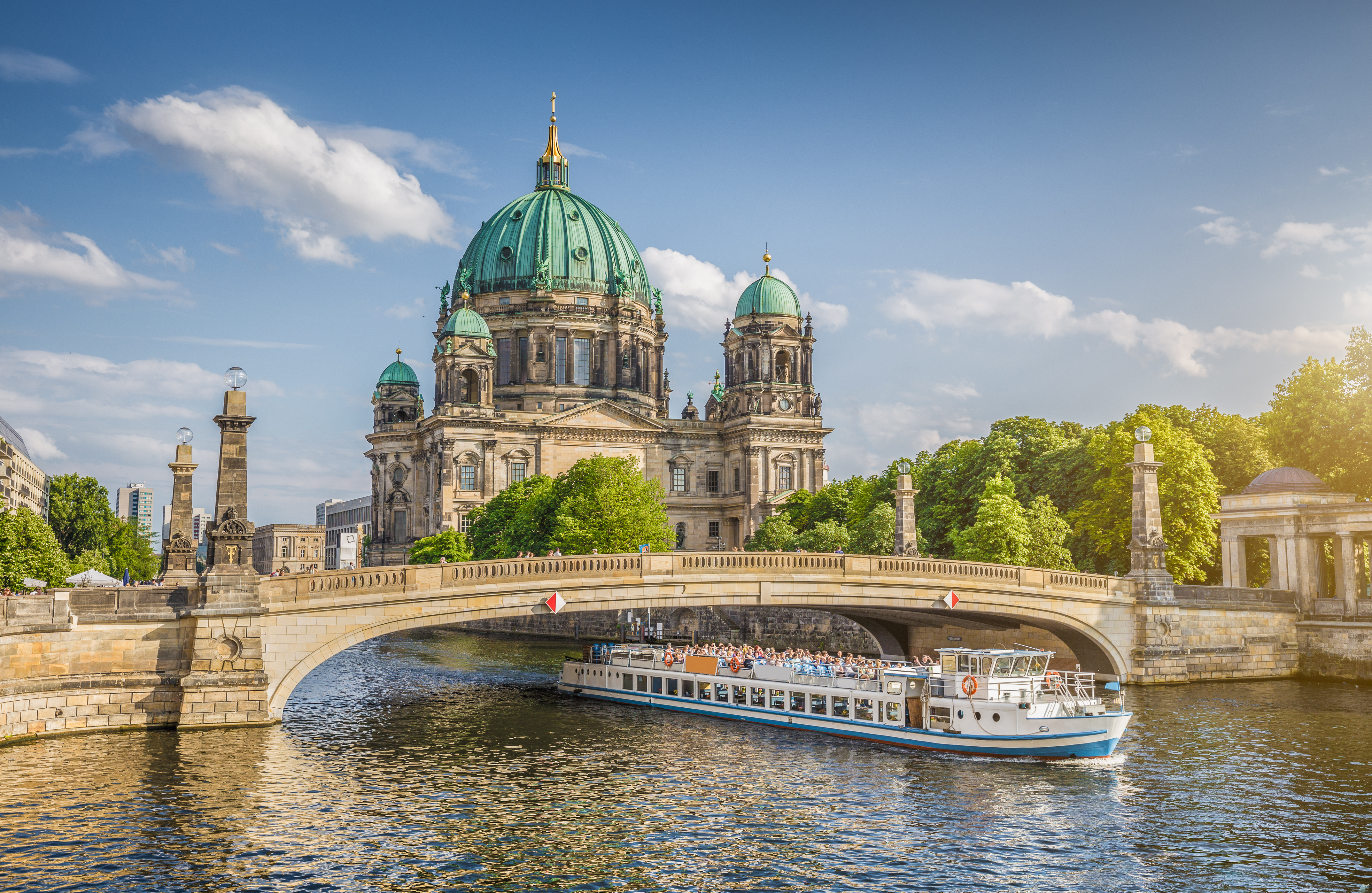 Imponerende Berlin Domkirke med grønne kupler og sightseeingbåd på Spree floden i solskin